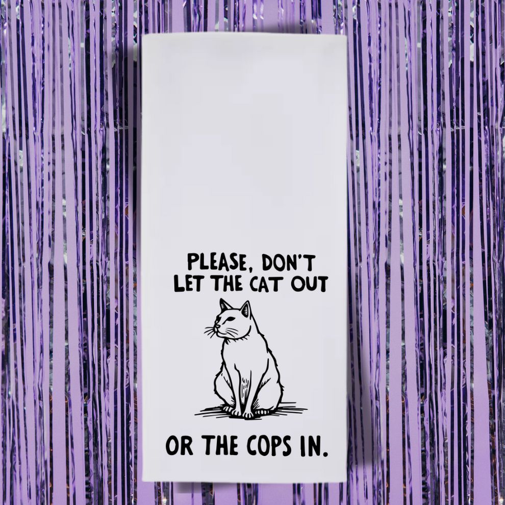 A white rectangular sign or towel with black text and a cat illustration, set against a background of purple metallic tinsel fringe. The text reads: "PLEASE, DON'T LET THE CAT OUT OR THE COPS IN." Between the sentences is a simple line-art drawing of a cat sitting and looking to the side.