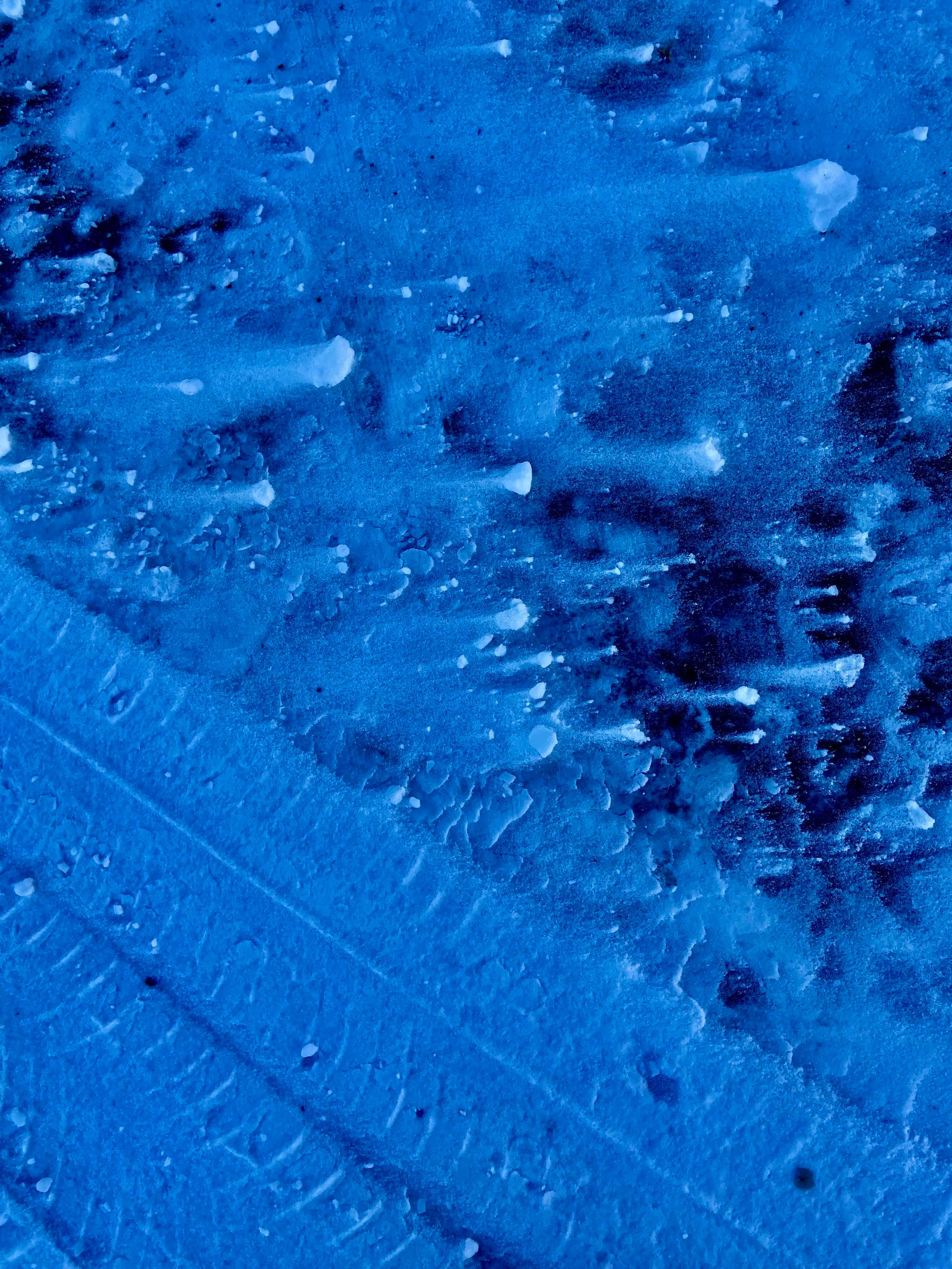 Snow on asphalt, blown by the wind and with wheel tracks crossing diagonally at the lower left. The photo has been edited to emphasize the blue tones and contrast. It looks like a lot of comets, with the snow clumps being the "comets" traveling to the right, and the "tails" being the snow that was blown to the left. 