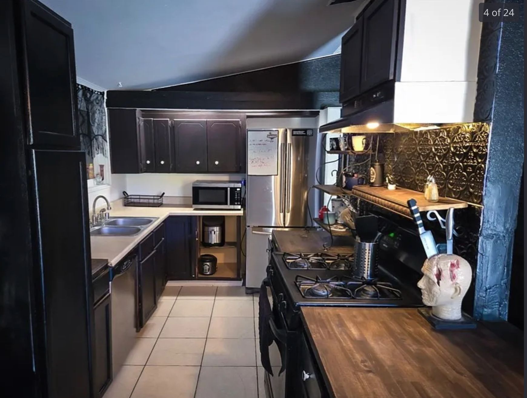 A kitchen with black cabinets and a black textures backsplash, and a knife holder that is a model of a human head with blood coming out of where the knives are stabbed. 