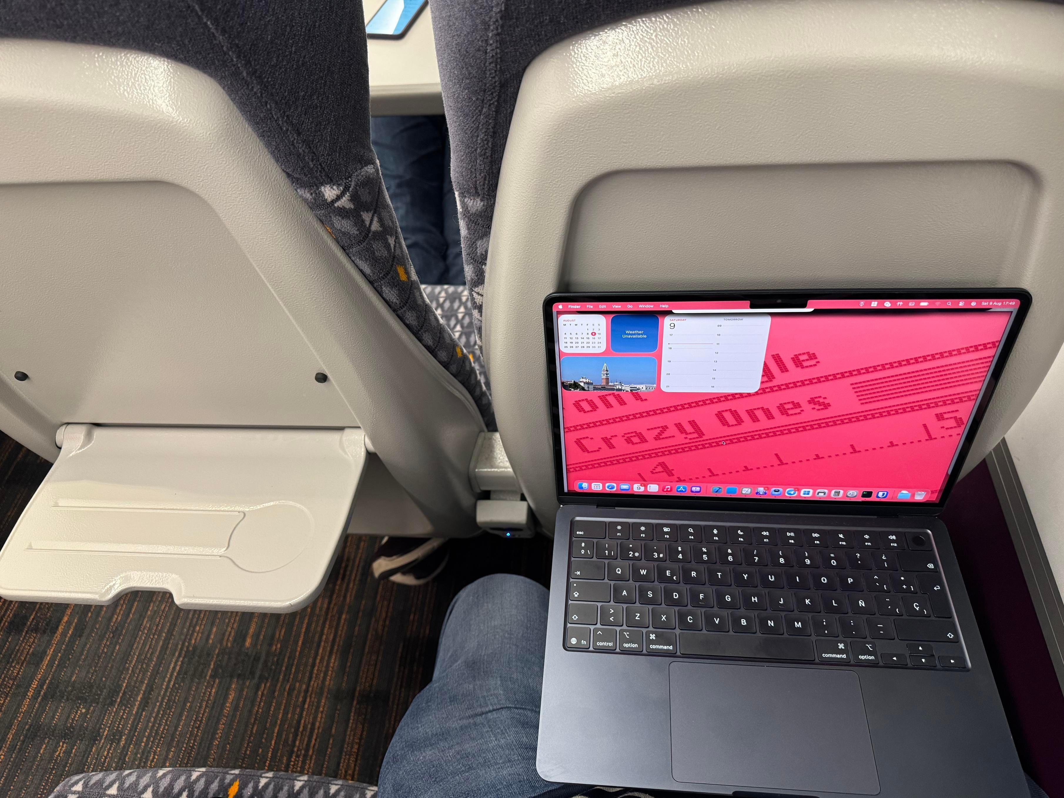 The distinctly tiny seat back tables, with my laptop open for comparison. You can see a small light between the seats, where the sockets are.