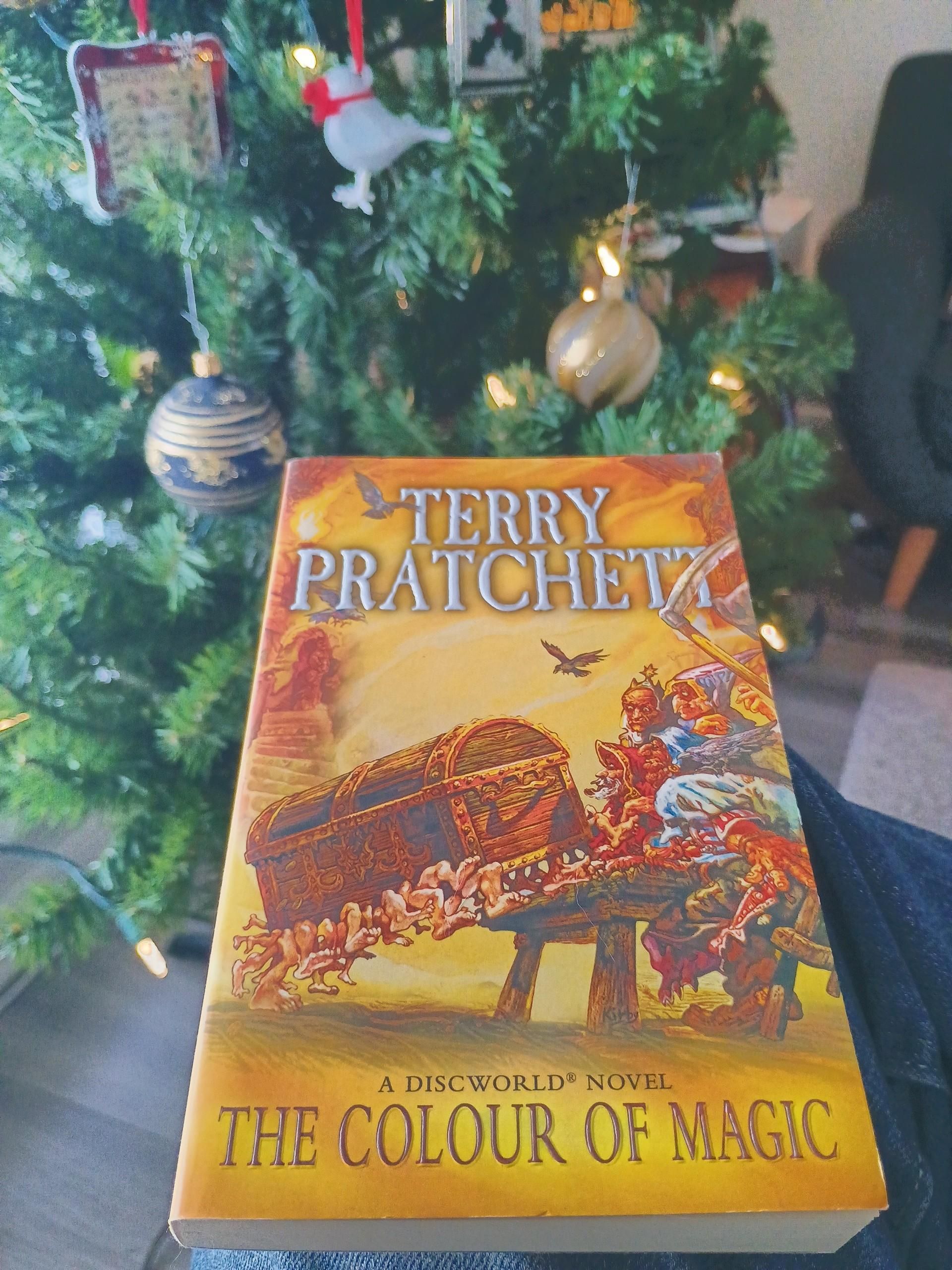 A copy of a softcover book with the tree behind. The book is Terry Pratchett's "The Colour of Magic" the first of the series.