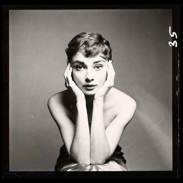 Audrey holds her head in her hands as she stares at the camera. 