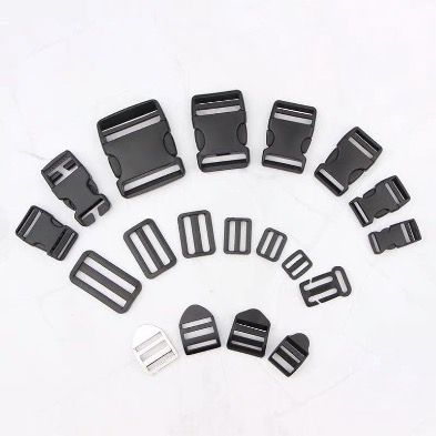A collection of black plastic side release buckles spread out in an array. These are the type of buckles that you squeeze on the side and they open having three prongs