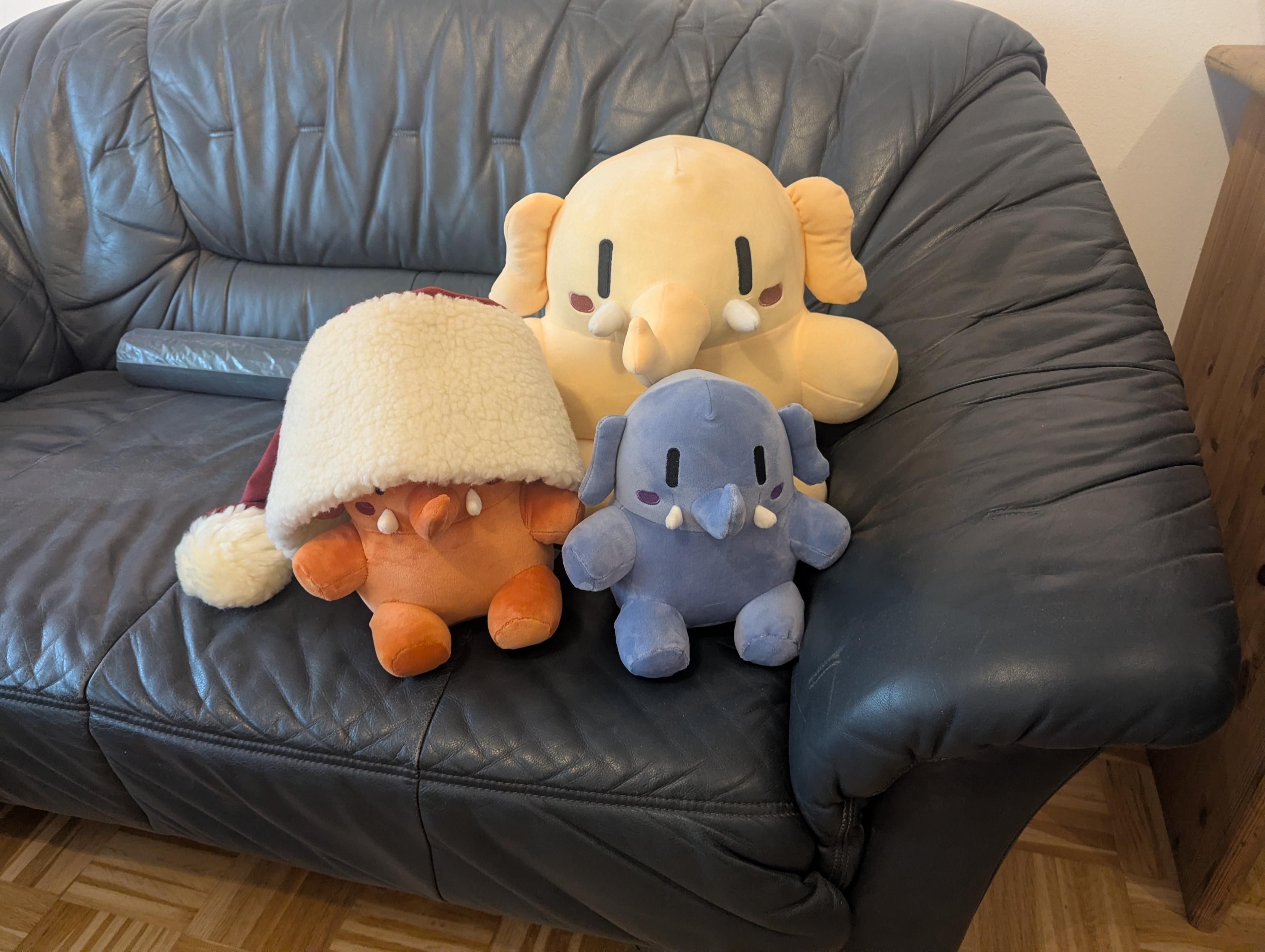 John, Joan and Jane Mastodon sitting on a dark blue'ish leather couch. Joan is wearing a santa's hat that's way too big for her.
