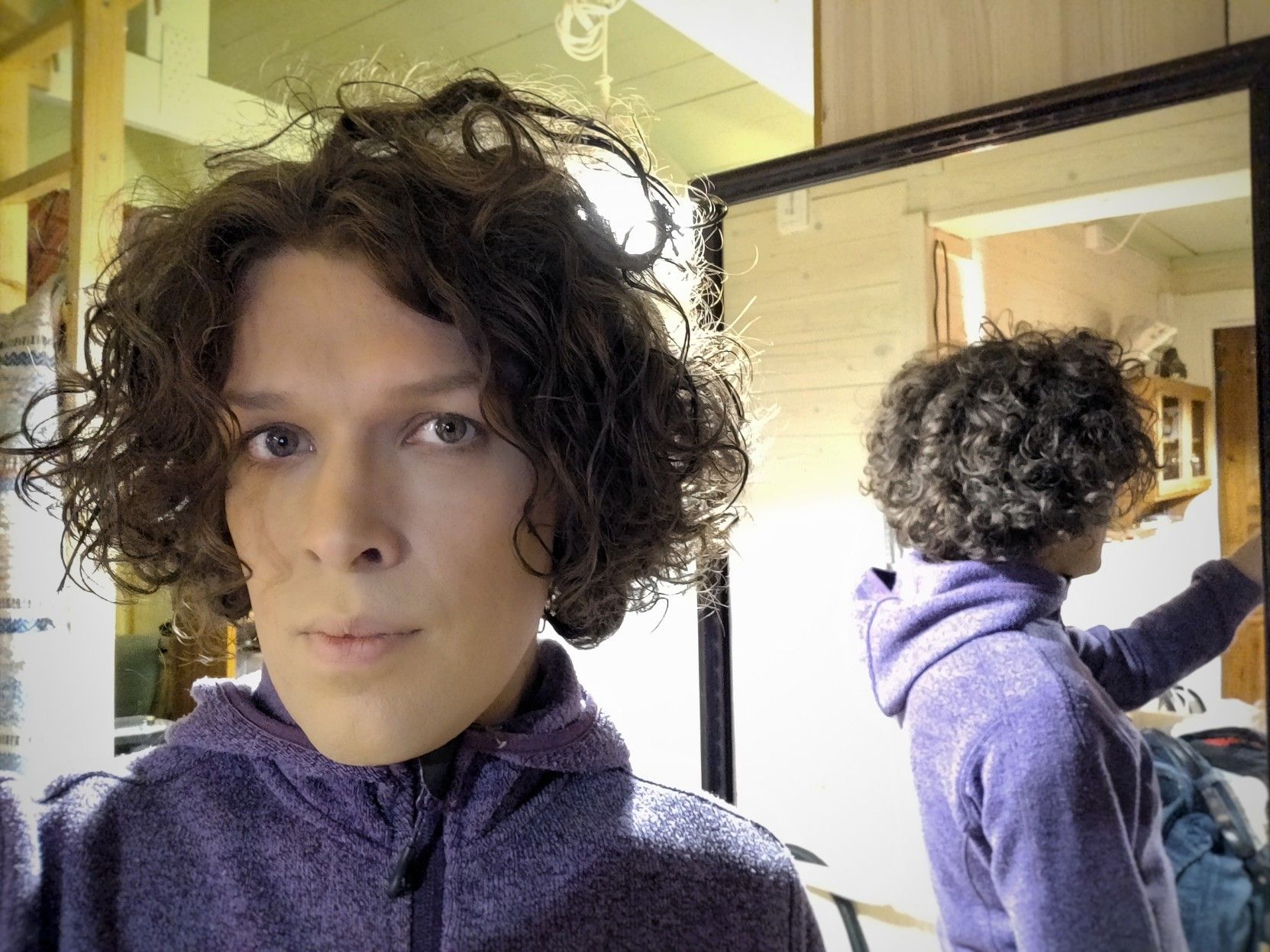 Selfie taken with mirror behind me, so that you can also see me from the side. I have a quite serious expression on my face. I'm wearing a purple hoodie.