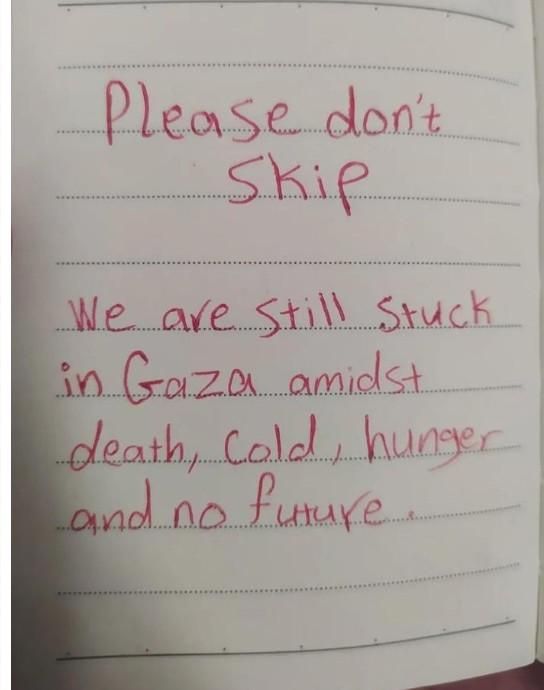 Texte écrit au stylo rouge sur un cahier ligné : "we are still stuck in Gaza amidst death, cold, hunger and no future.