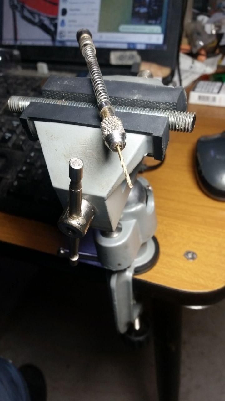 Morsa snodata fissata all'angolo del tavolo.
Dentro c'è un pezzo di barra filettata M10, sopra un trapanino a siringa con una punta da 1,5 mm.