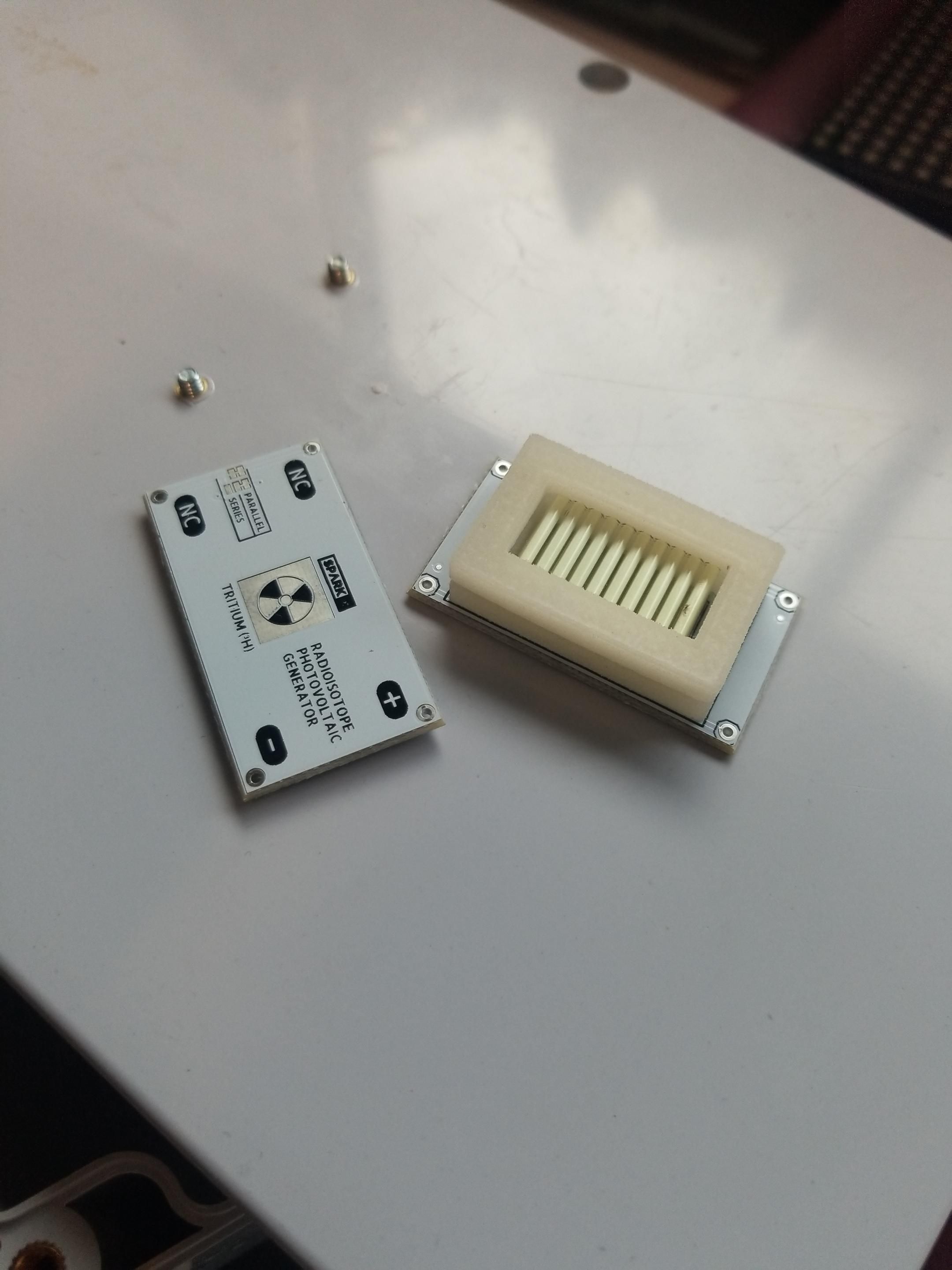 A row of tritium glow vials suspended in a rubber gasket next to a PCB with a trefoil on it