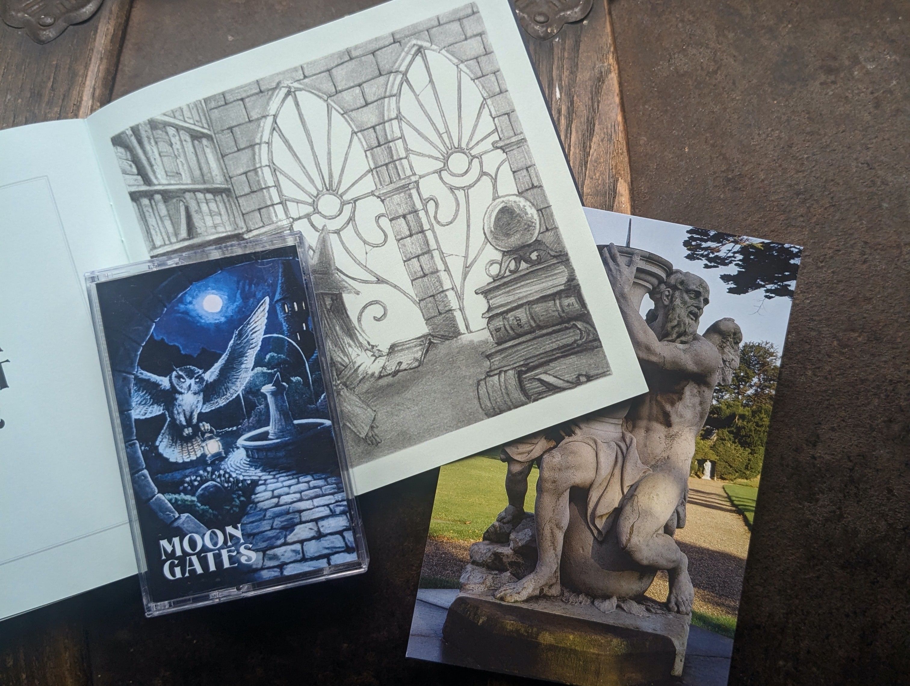 photo of the tape version of the aura merlin album "Moon Gates" with the accompanying booklet showing a detailed pencil drawing of a wizard in their study