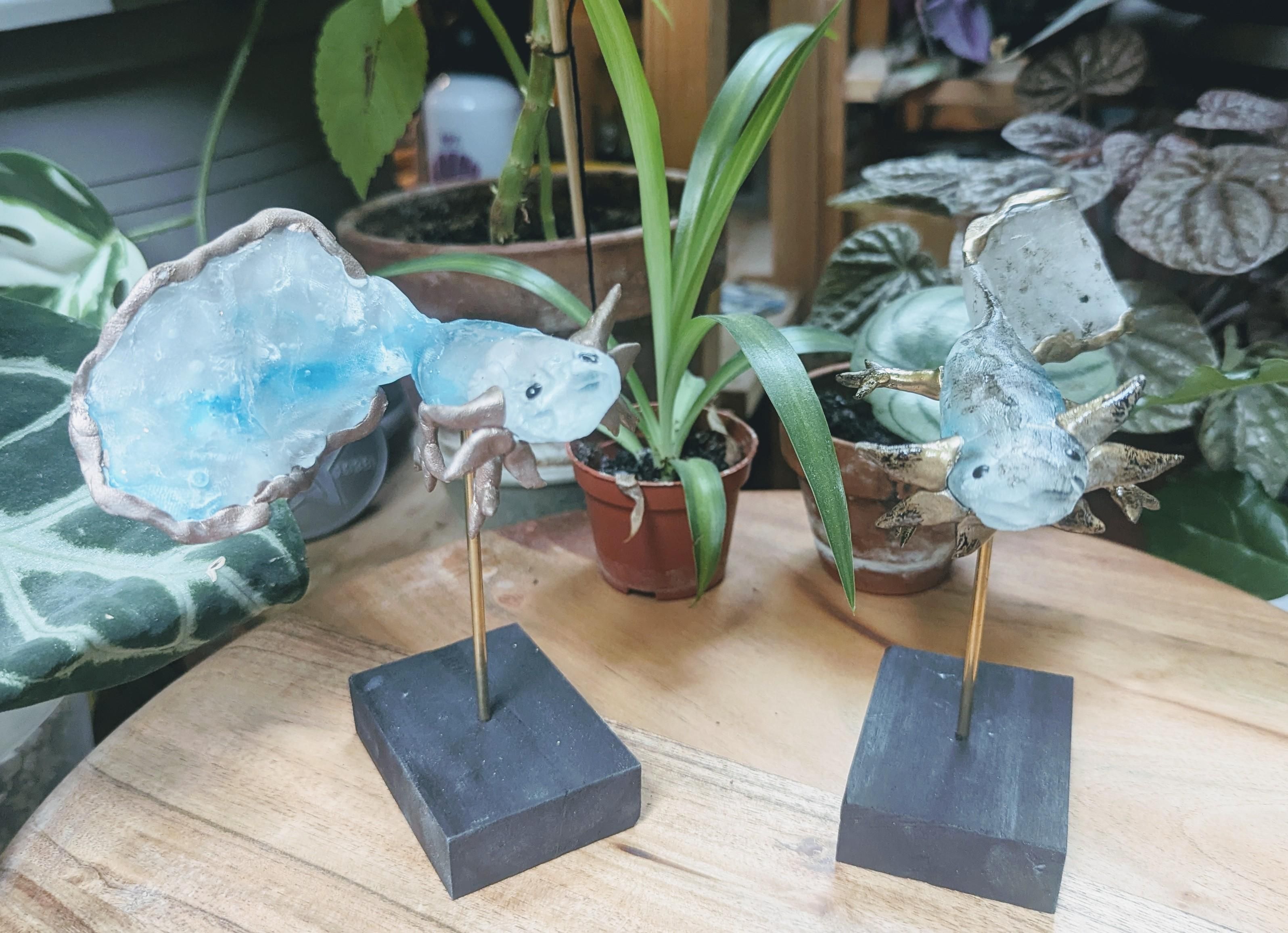 2 petits axolots en verre sur socles, leur branchies pattes ont des touche dorée pour l’un et rose-doré pour l’autre. l’axolot doré a de la peinture au goudron sur son dos en guise de tâches