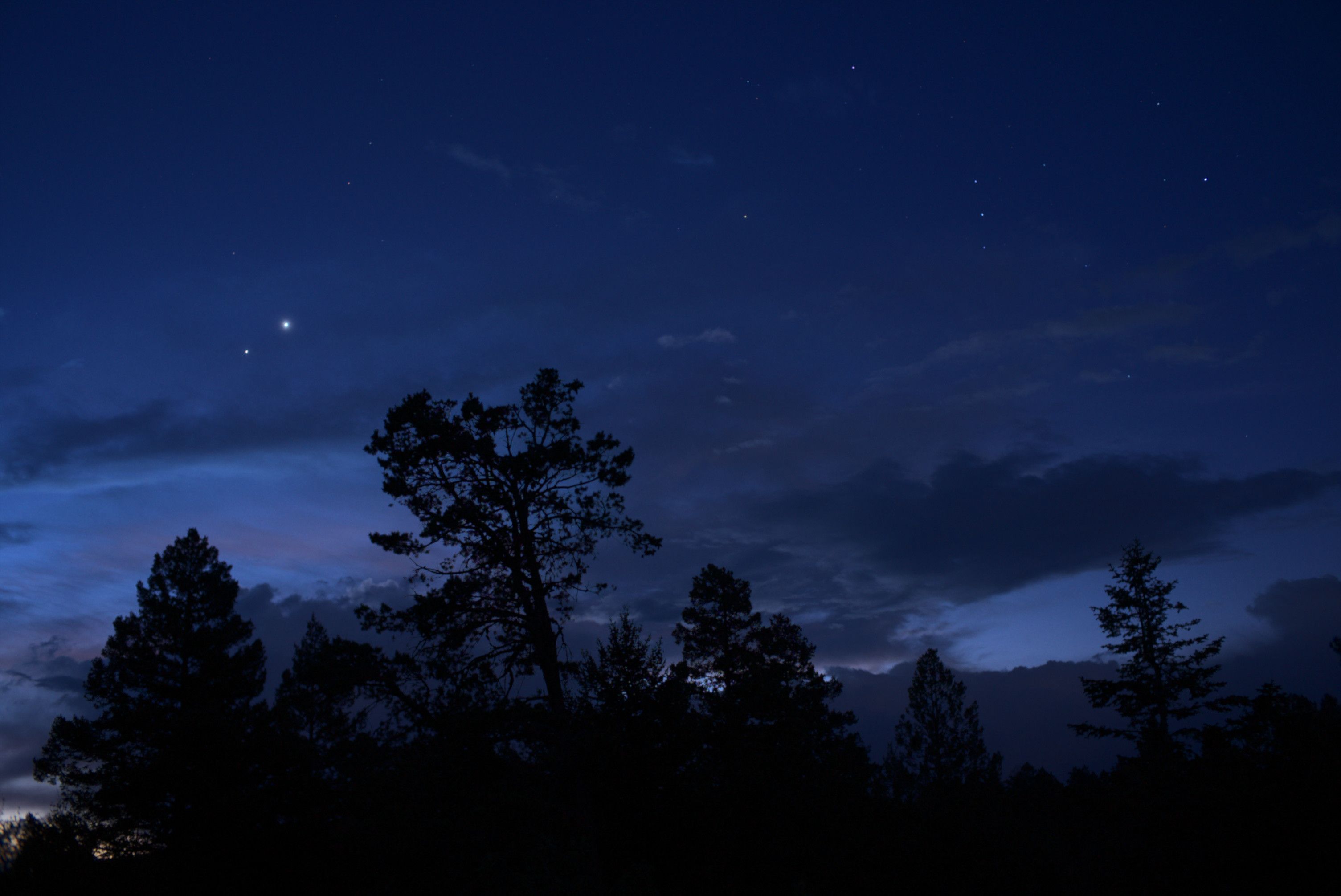 Jupiter and Venus shine brightly as the get closer to each other in the pre-dawn sky.

Orion is in the right half of the frame.

Trees are dark silhouettes. 

Scattered clouds add texture to the sky.