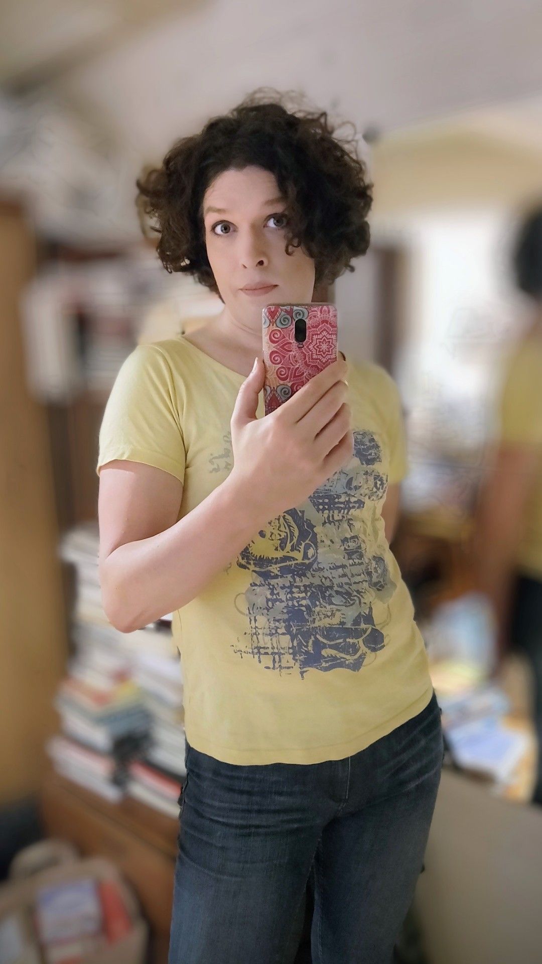 Mirror selfie in tight blir jeans and a yellow t-shirt with a blue pattern.