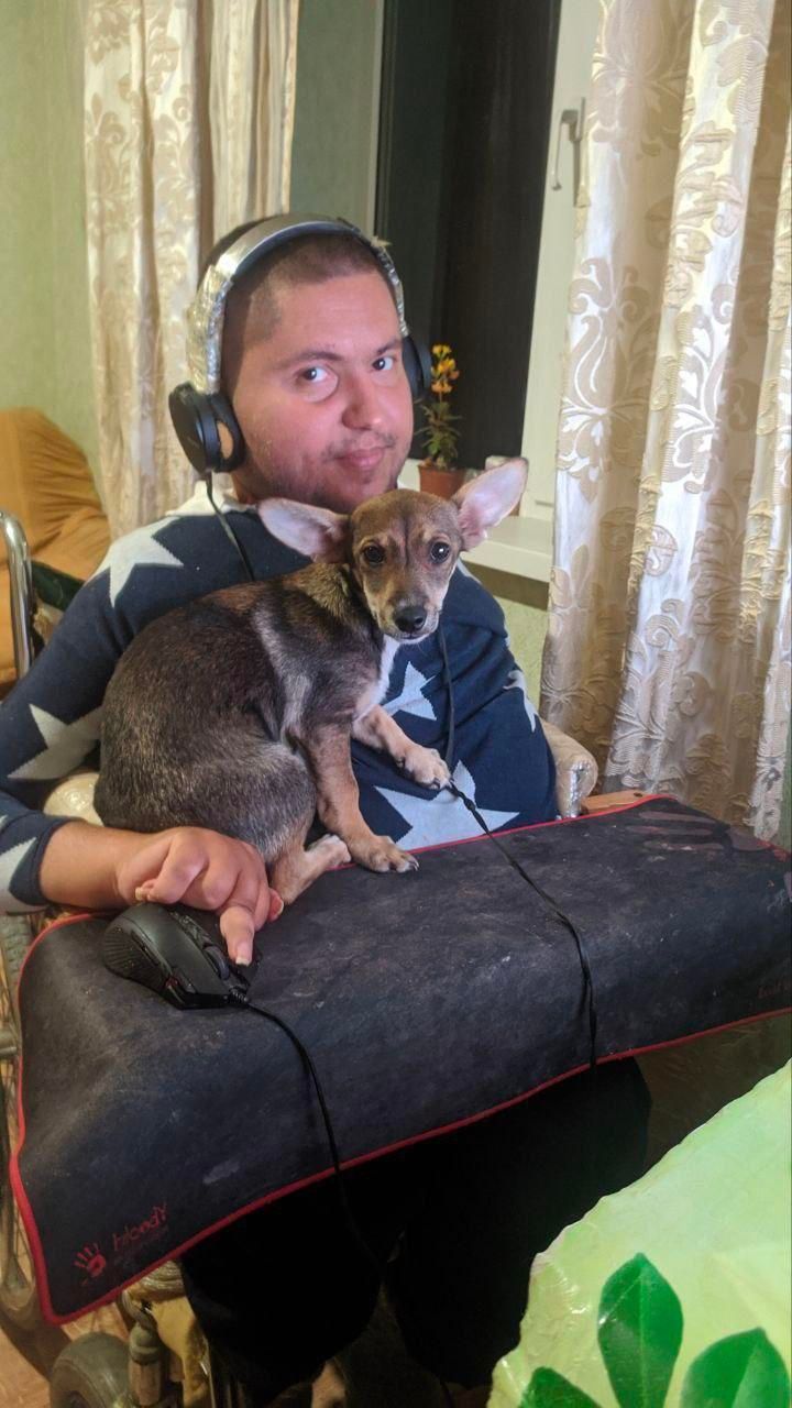 a dark haired man in a power wheelchair with a little dog in his lap, with matching soulful gazes