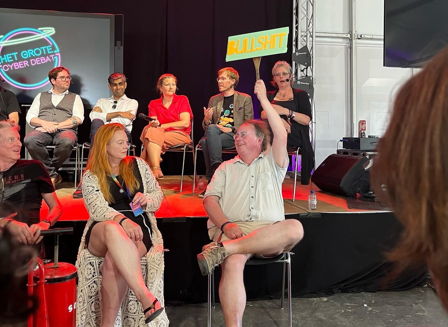 panel of politicians with on a lower level three people in chairs. Bert on the right holding a sign saying "BULLSHIT"
