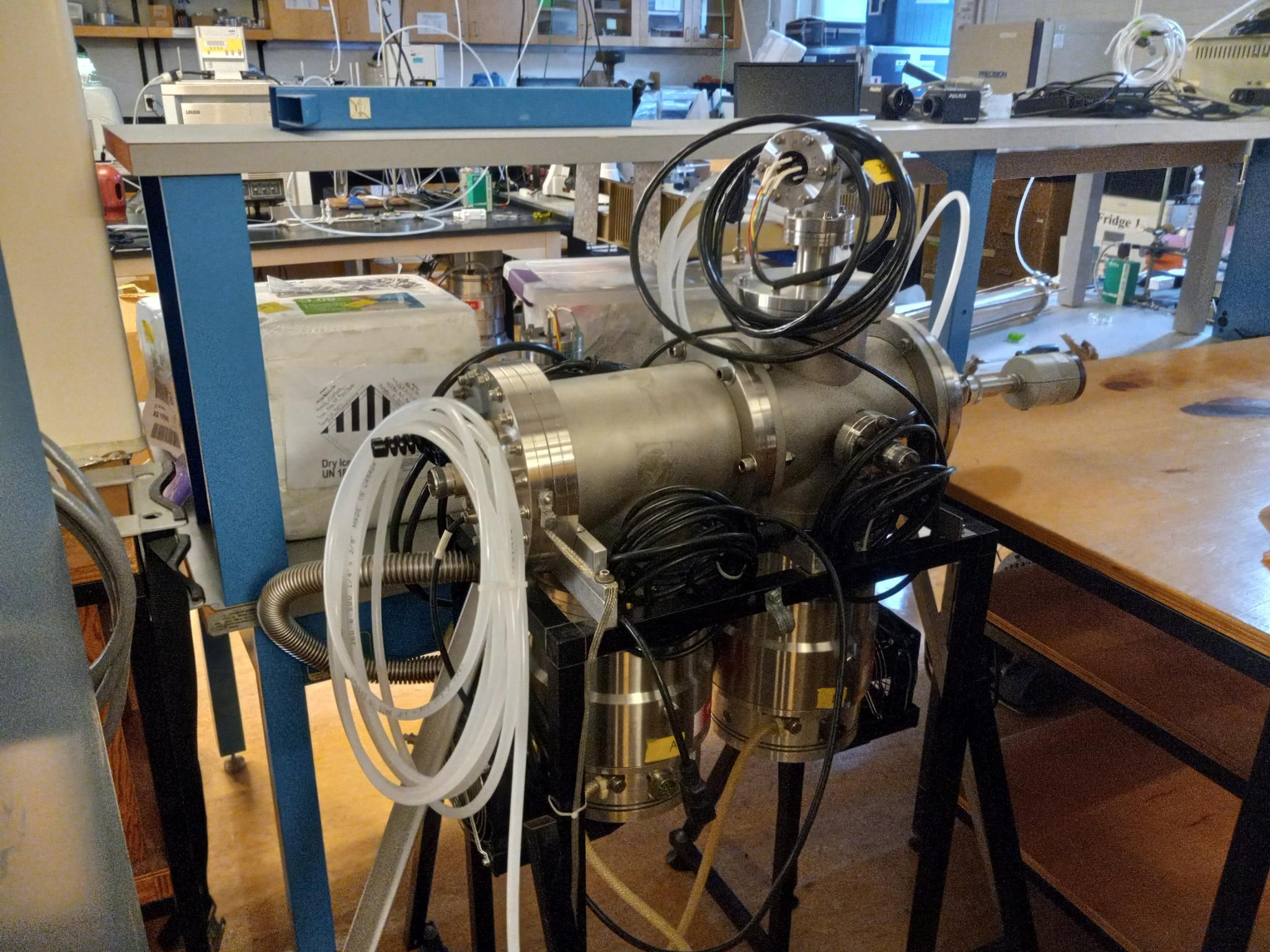 A picture of a cool piece of very complicated chemistry equipment.  It's a metal cylinder with a lot of tubes.  There's a lot of other complicated, interesting-looking chemistry stuff in the background in the lab. 
