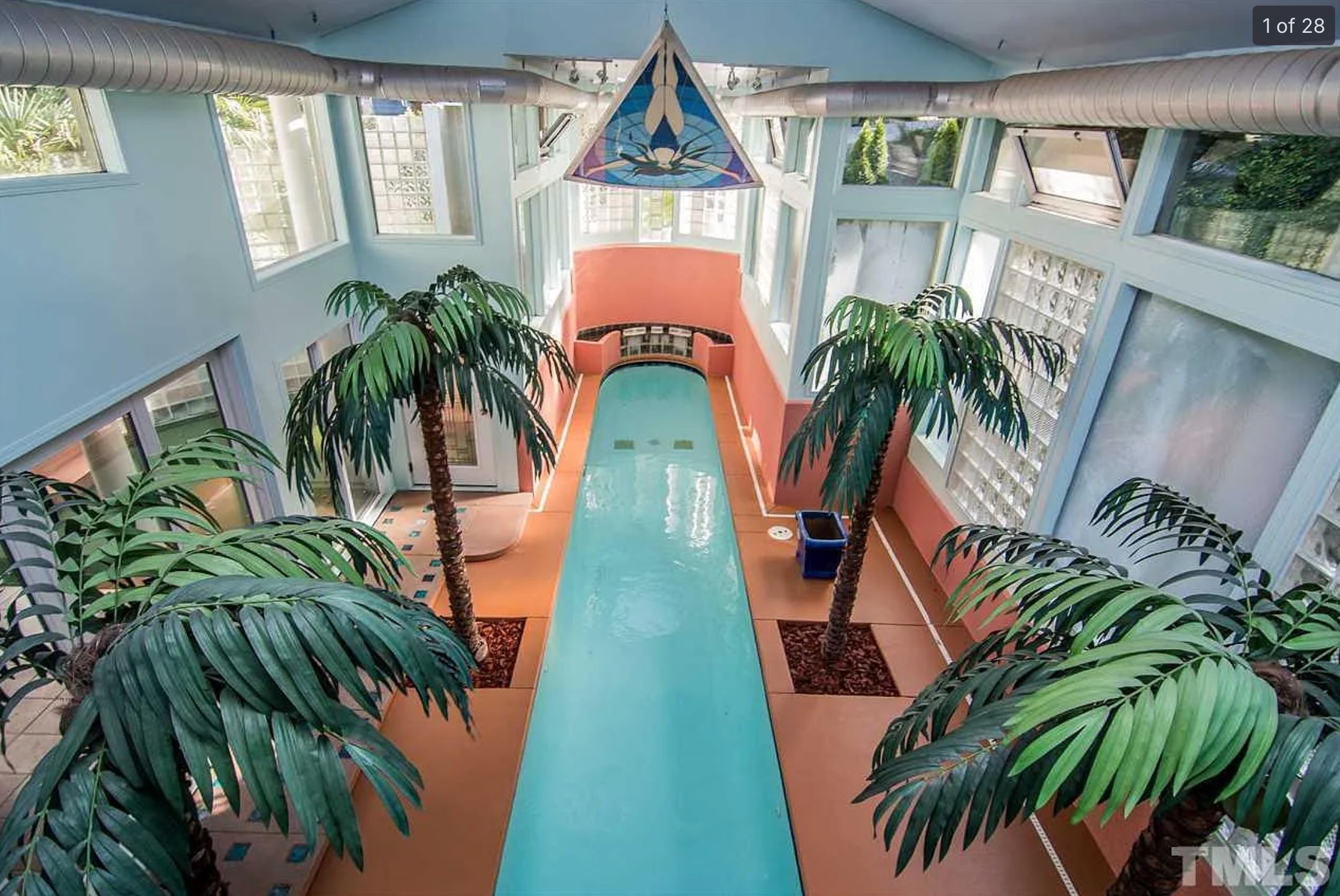 An indoor pool that is very long and narrow and round at the end, with fake palm trees along either side and a triangle banner hanging down of a woman diving into a pool. 