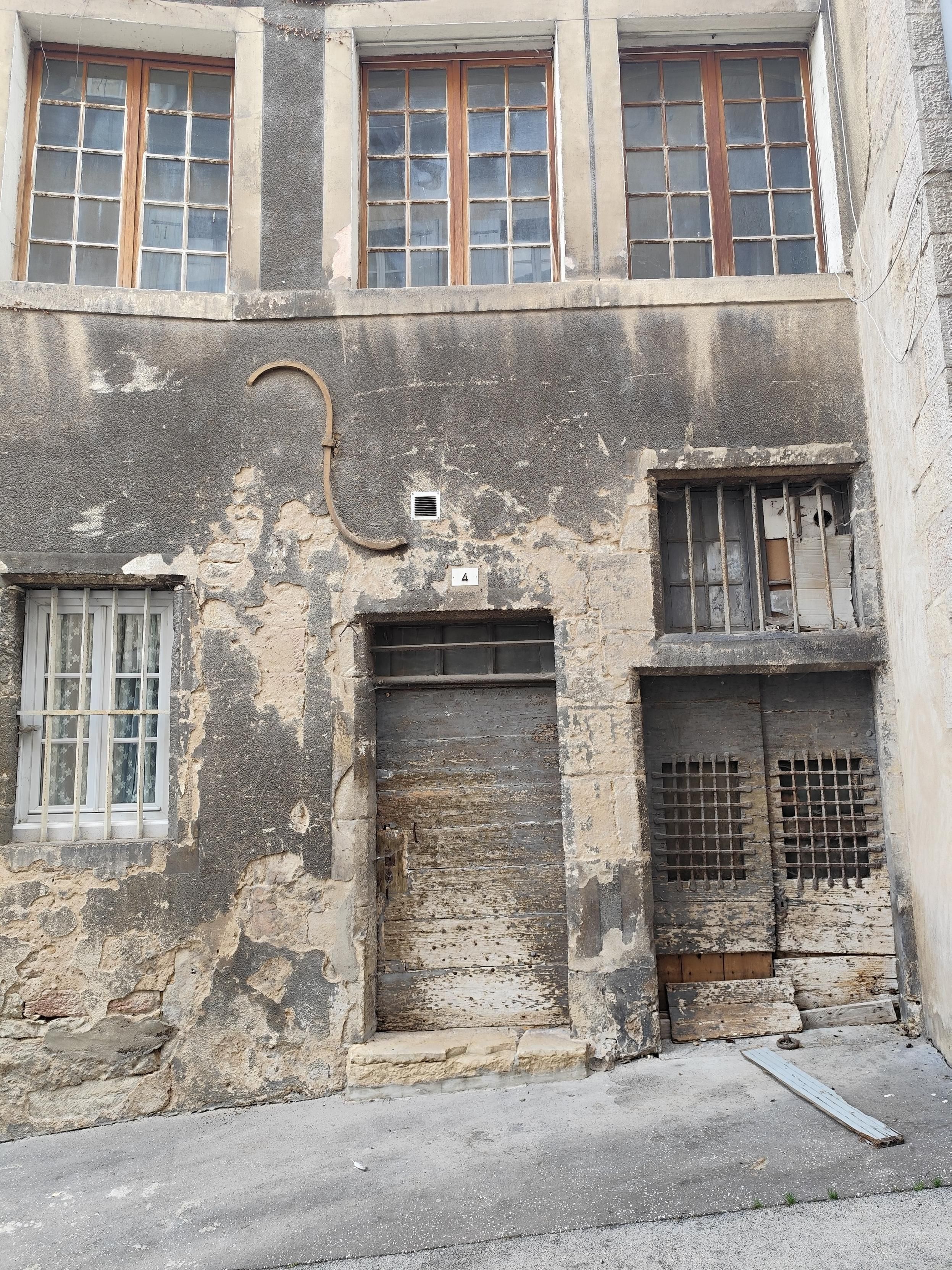 Graubeige dreckige Hausfassade mit drei alten Industrie Sprossenfenstern im 1.OG und zwei alten Holztüren zur Straße.