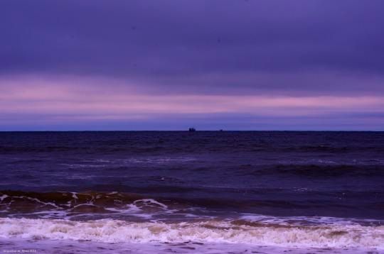 A photo of the Atlantic Ocean with a ship in the distance, horizon about midway in the frame. The colors have been shifted towards purple. So it looks like a different world.