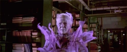 Ghost woman librarian from the movie Ghostbusters. She is an old woman that looks angry and is the color purple. She has shelves of books behind her. She is moving forward, and she turns into a skelton face.
