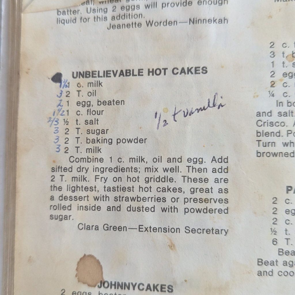 Cookbook page stained from use featuring a recipe for hot cakes with handwritten ingredient adjustments in pen.