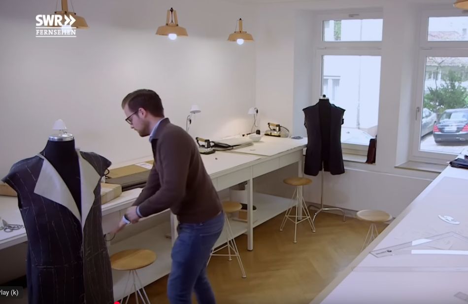 Tailor in his workspace, with bright lights and high desks, forms
