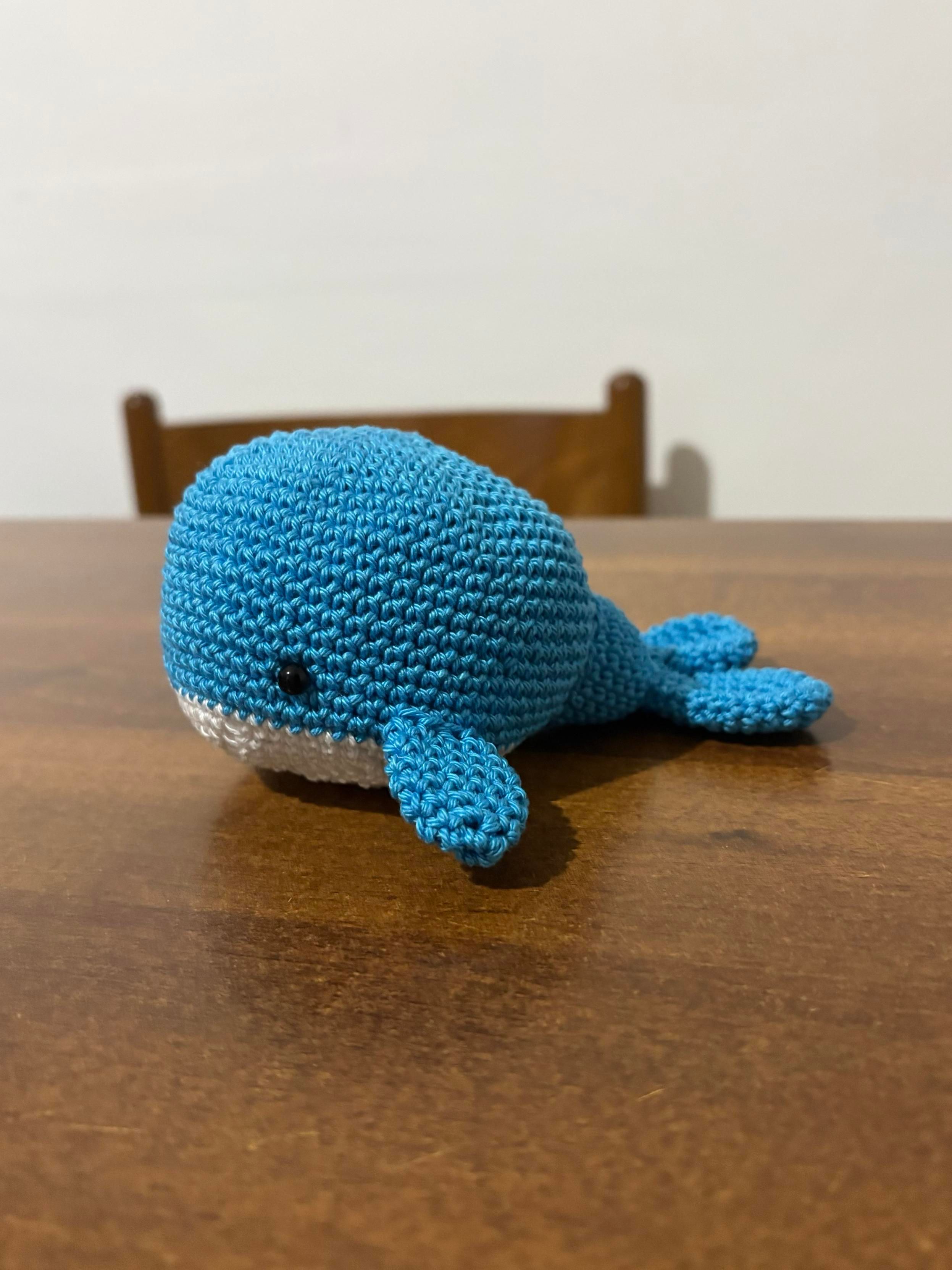 Primo piano di una balena amigurumi fatta all’uncinetto con dorso azzurro e ventre bianco