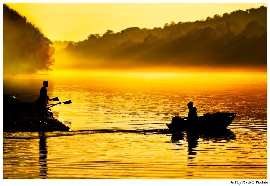 Photograph of bright golden light on the river with a boat leaving the dock while a man stands on the nearby pier. The boat and the people are all in dark silhouette. 