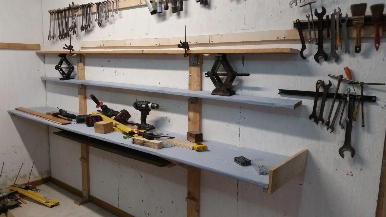 Scaffale con un ripiano grande, rivestito con vecchi manifesti capovolti, e due piccoli sopra, uno rivestito e uno grezzo.
Quello più in alto è sorretto con due cric a parallelogramma.
