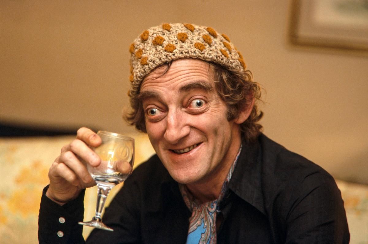 Head and shoulders informal portrait of a smiling man with big cross eyes holding a wine glass.