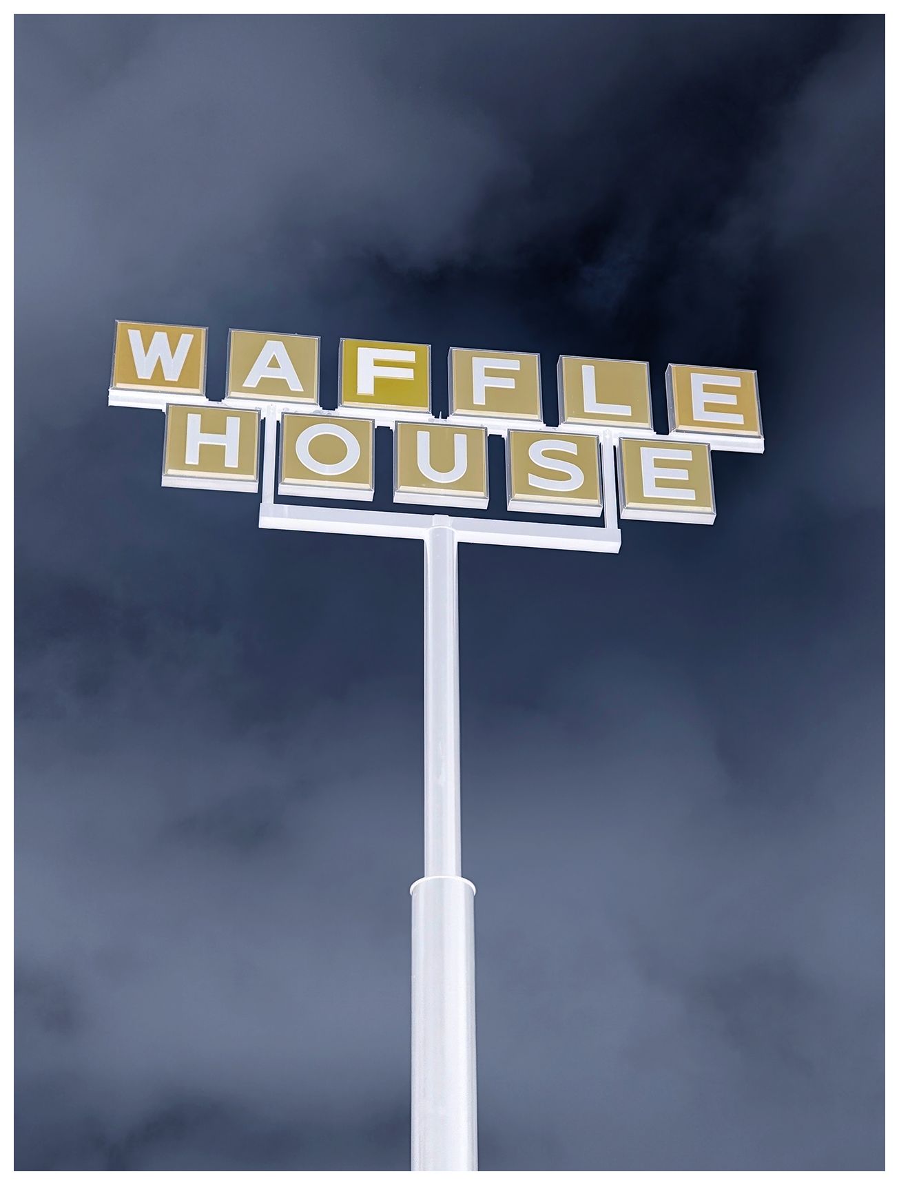 ai-assisted alt text:

inverted/recolored.

A tall white pole displays yellow block letters spelling WAFFLE HOUSE against a dramatic, cloudy dark sky in the background. The sign is seen from below, emphasizing its height and making the letters stand out boldly.
