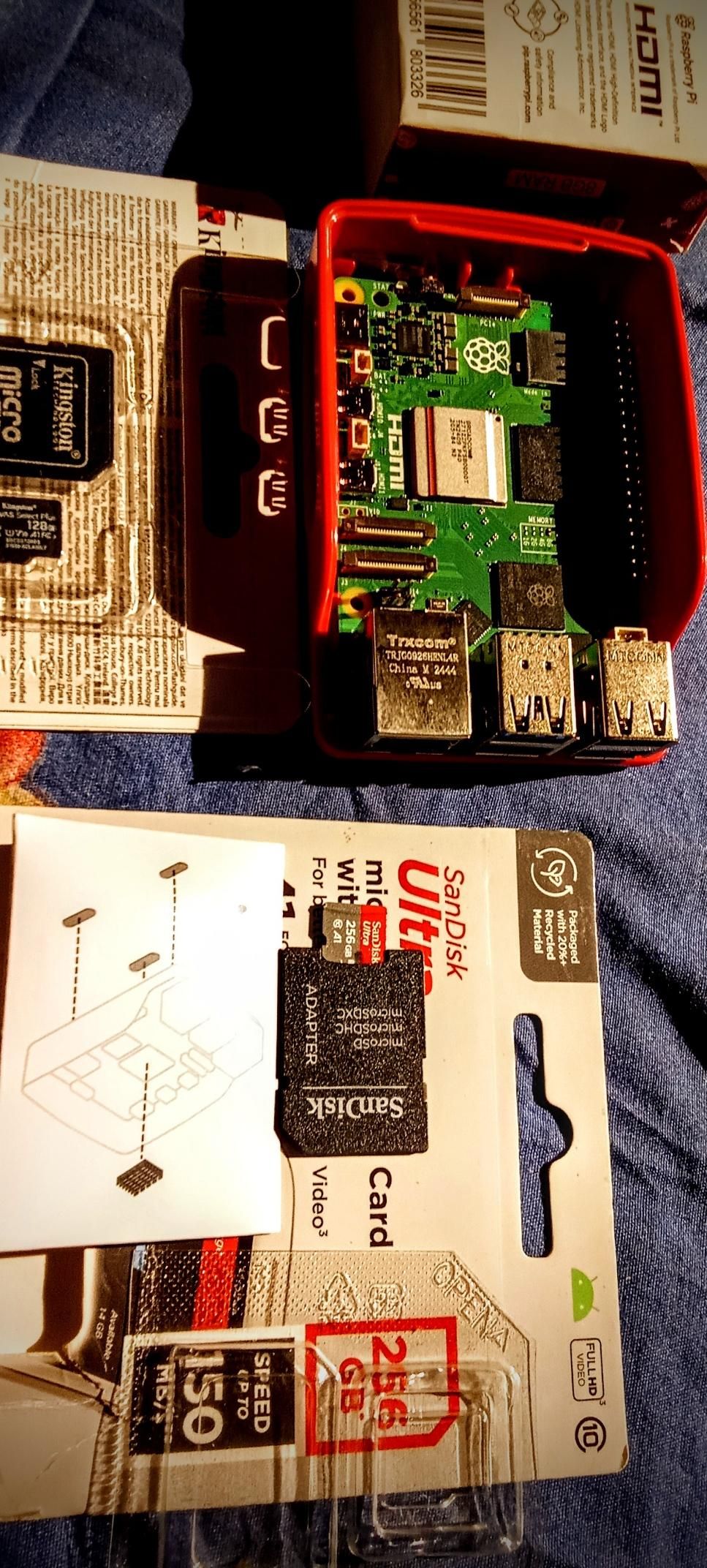 The image shows a Raspberry Pi 5 8GB in a Red White optional plastic case, with the lid open to reveal the green circuit board. The board features various components, including the Broadcom SoC, USB ports, Ethernet port, and HDMI port. A SanDisk Ultra microSD card is visible, packaged in a clear plastic holder with a white backing. The card is labeled "256GB" and "UHS-I," with a speed rating of "150." The packaging also includes a diagram showing the card's placement in the Raspberry Pi. The background is a blue fabric surface, and the Raspberry Pi box is partially visible, with text indicating "HDMI" and "Raspberry Pi."

 Ovis2-8B

🌱 Energy used: 0.185 Wh