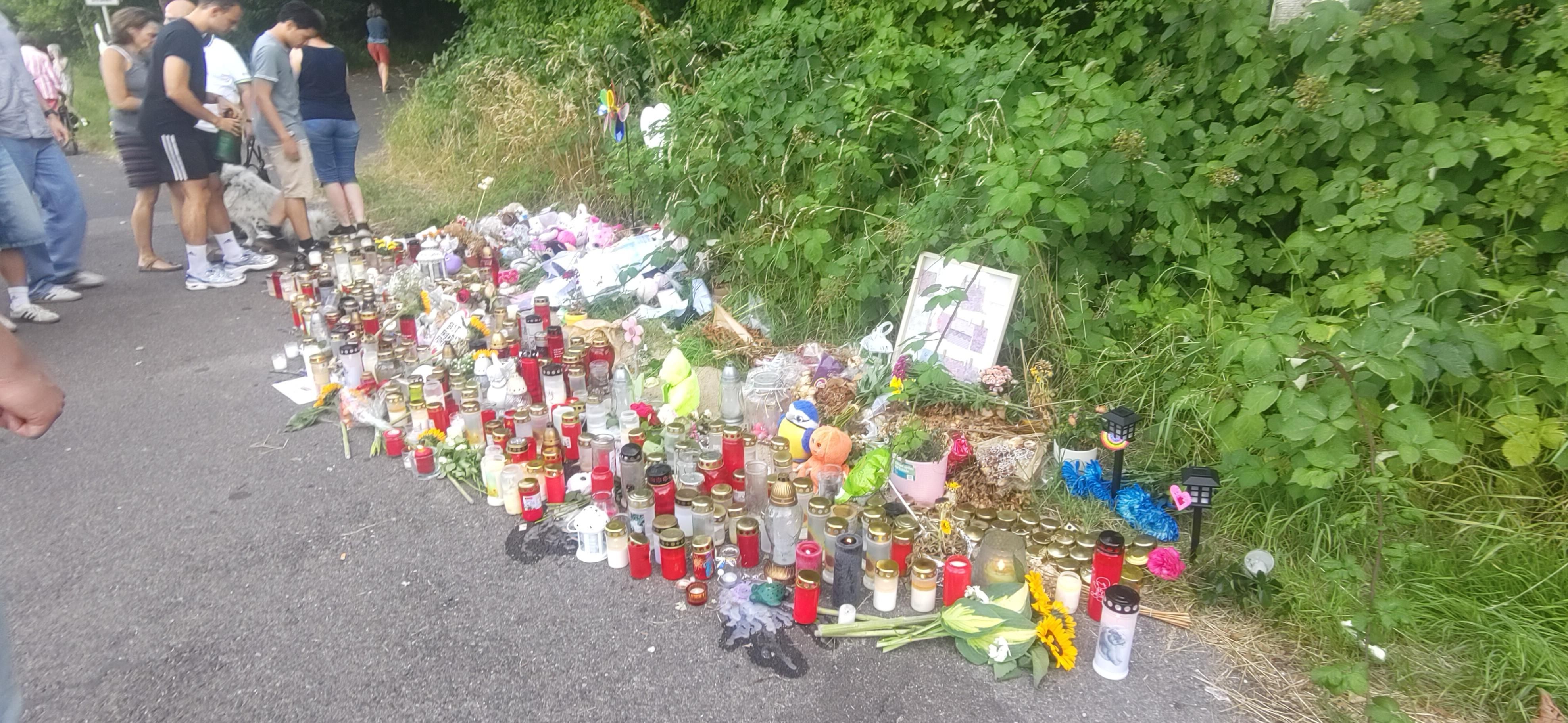 Über mehrere Meter sind Andenken, Blumen, Schriftstücke, (Grab)kerzen u.a. auf dem Wegrand verteilt.