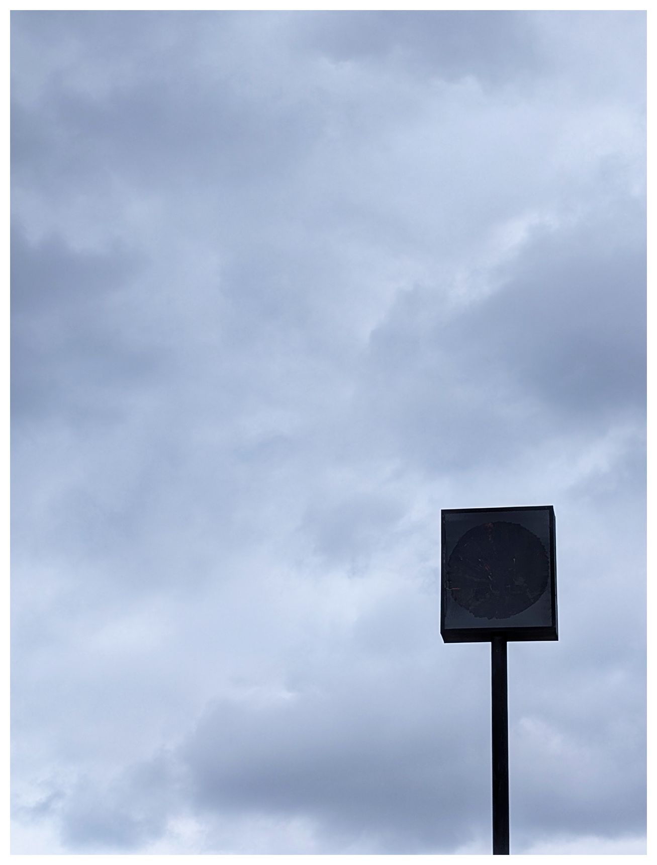 ai-assisted alt text:

the top of a black, square sign stands on a stories-high pole against a cloudy, overcast sky. 