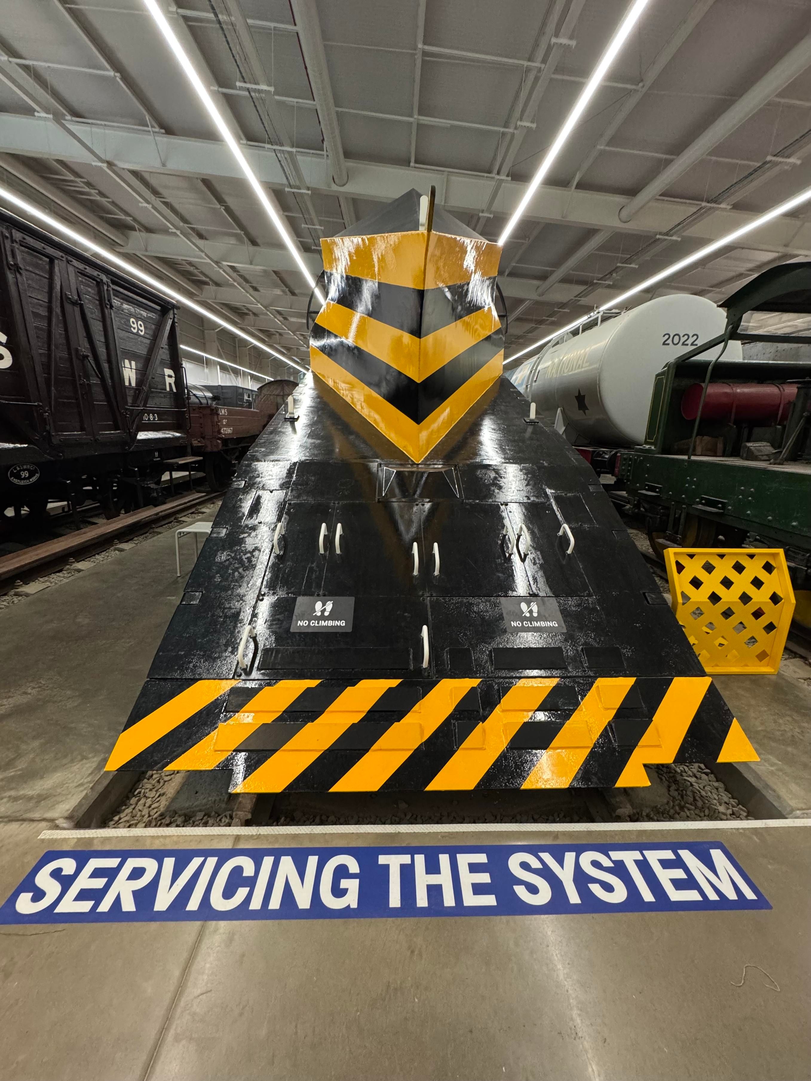 Front view of a ZZA Snowplough built by NER out of recycled railway tenders in 1965. In front of it a large sign painted on the floor says “SERVICING THE SYSTEM”