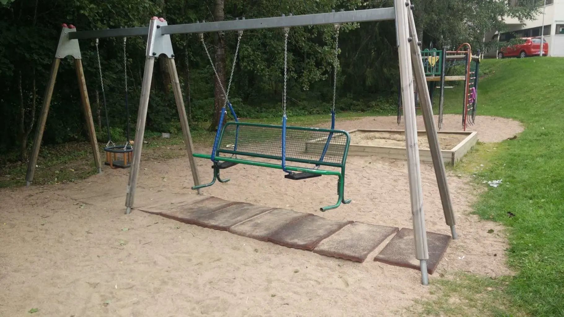 Puiston keinut johon on nostettu iso metallien puiston penkki