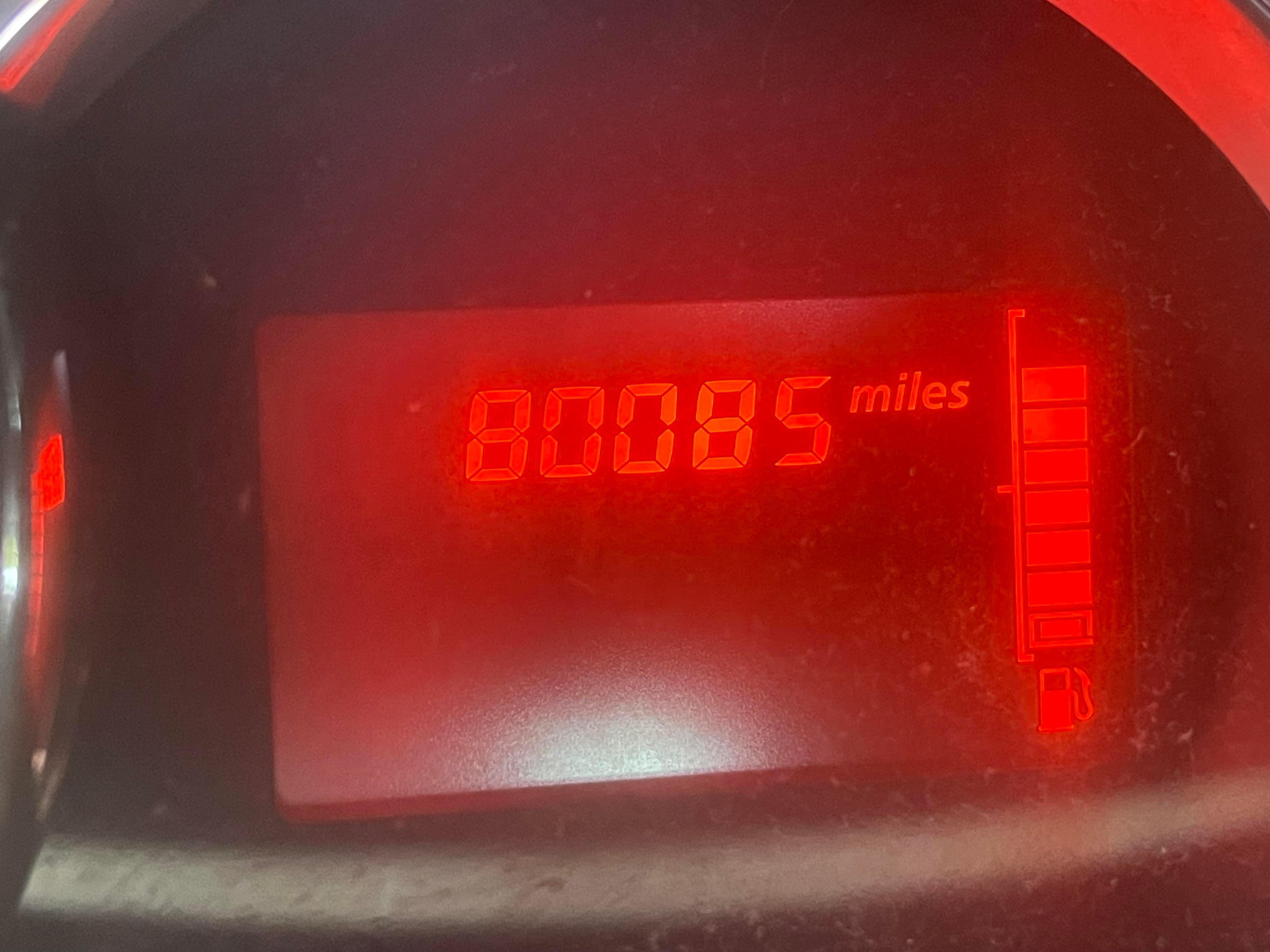 An orange segmented LCD car odometer showing 80085 miles