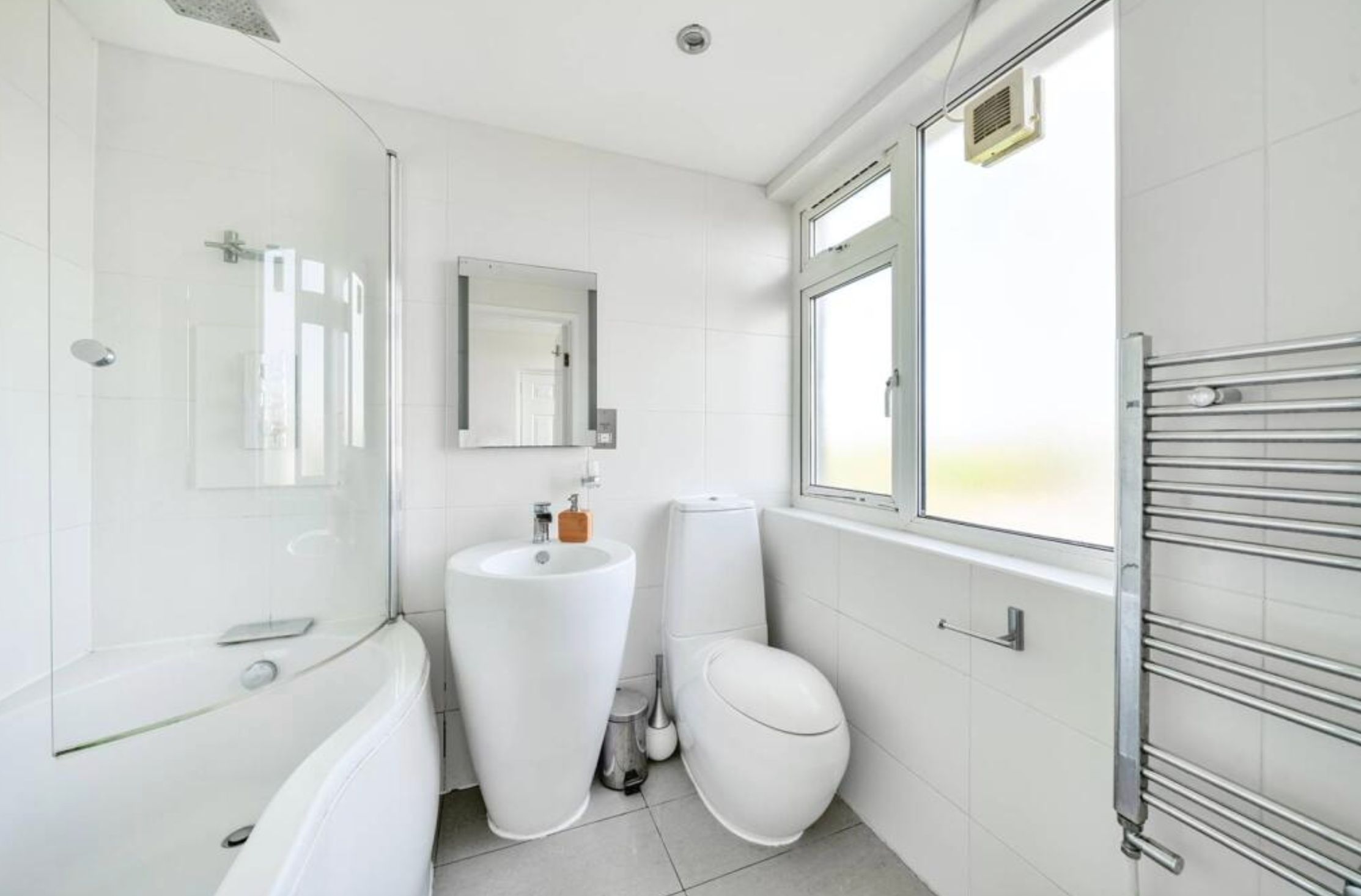 An all white bathroom with a toilet that looks long and very narrow. It is right next to the wall and is a bulbous round shape. 