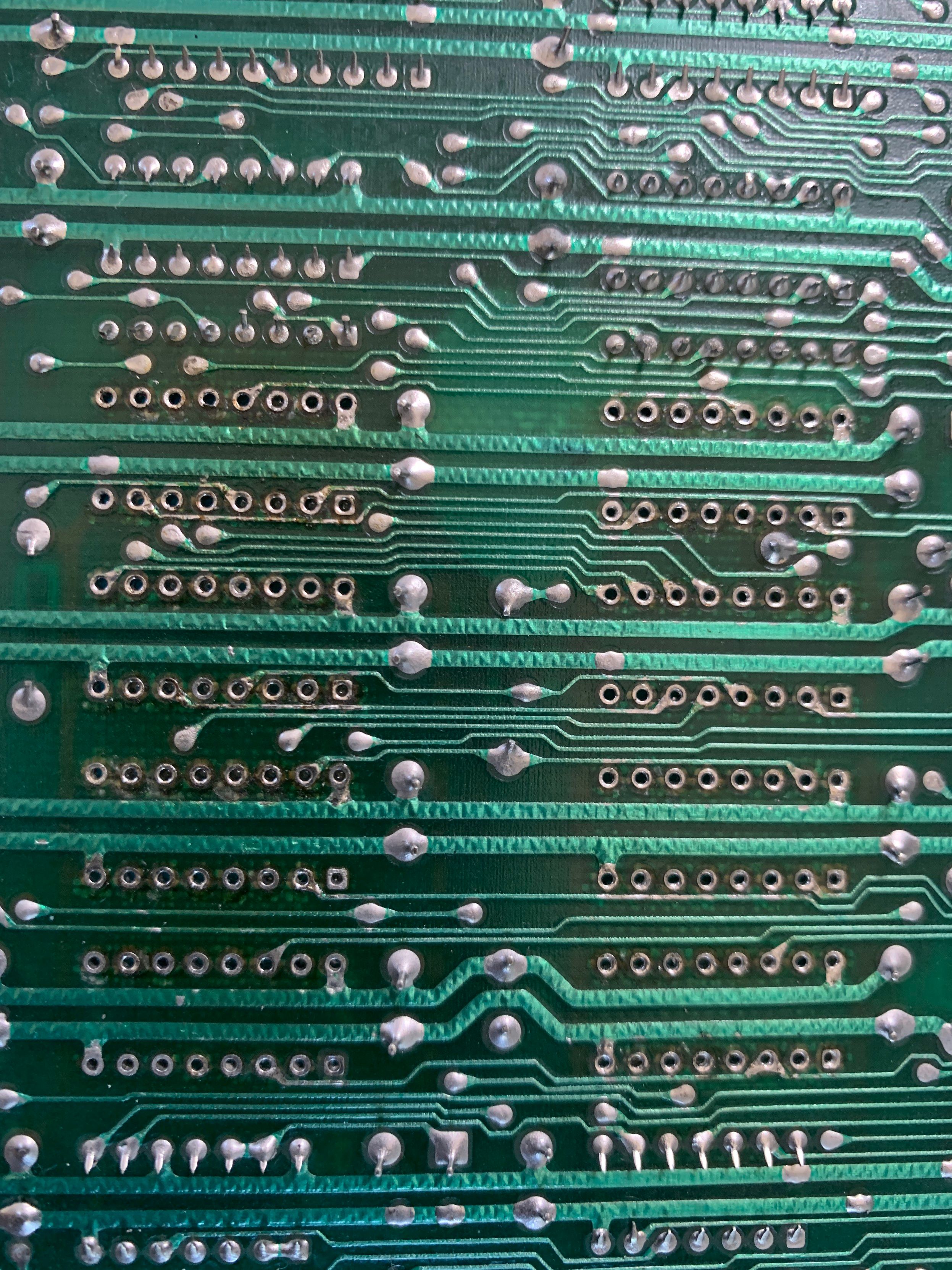 Reverse side of the C64 main board showing the through hole connectors for the 8 RAM sockets after the first pass of cleanup.   Green solder mask on the board throughout.