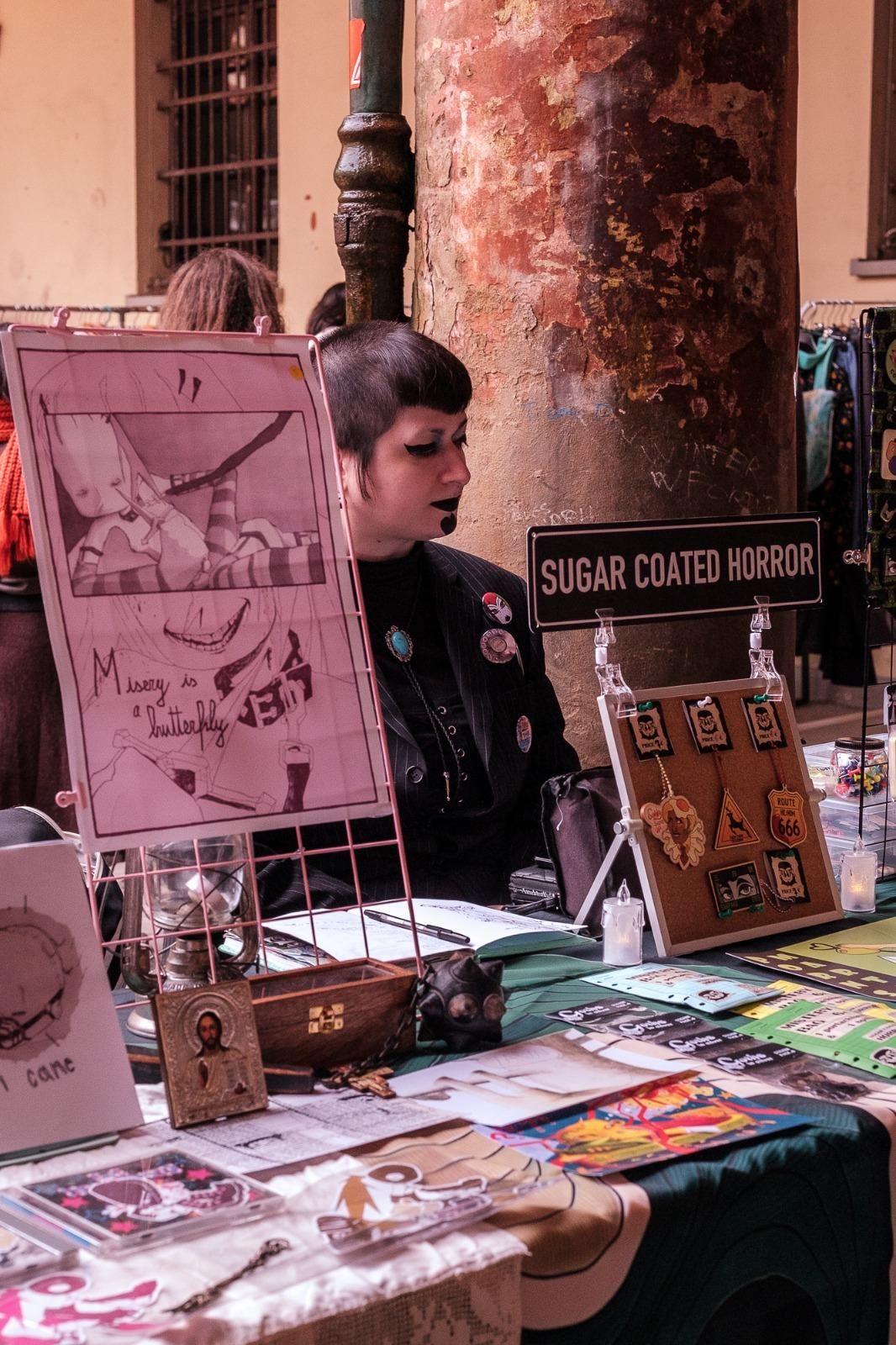 Evren è seduto dietro un banco presso un festival di autoproduzion indie, circondato da stampe illustrate, sticker, portachiavi e merch di sua produzione.
Espone un cartello con scritto “sugar soated horror”, il suo nome d'arte. 
Ha un look dark/alternativo con un trucco marcato. 
Atmosfera resa vintage dalla fotografa, Evren è sotto un portico con colonne consumate dal tempo.