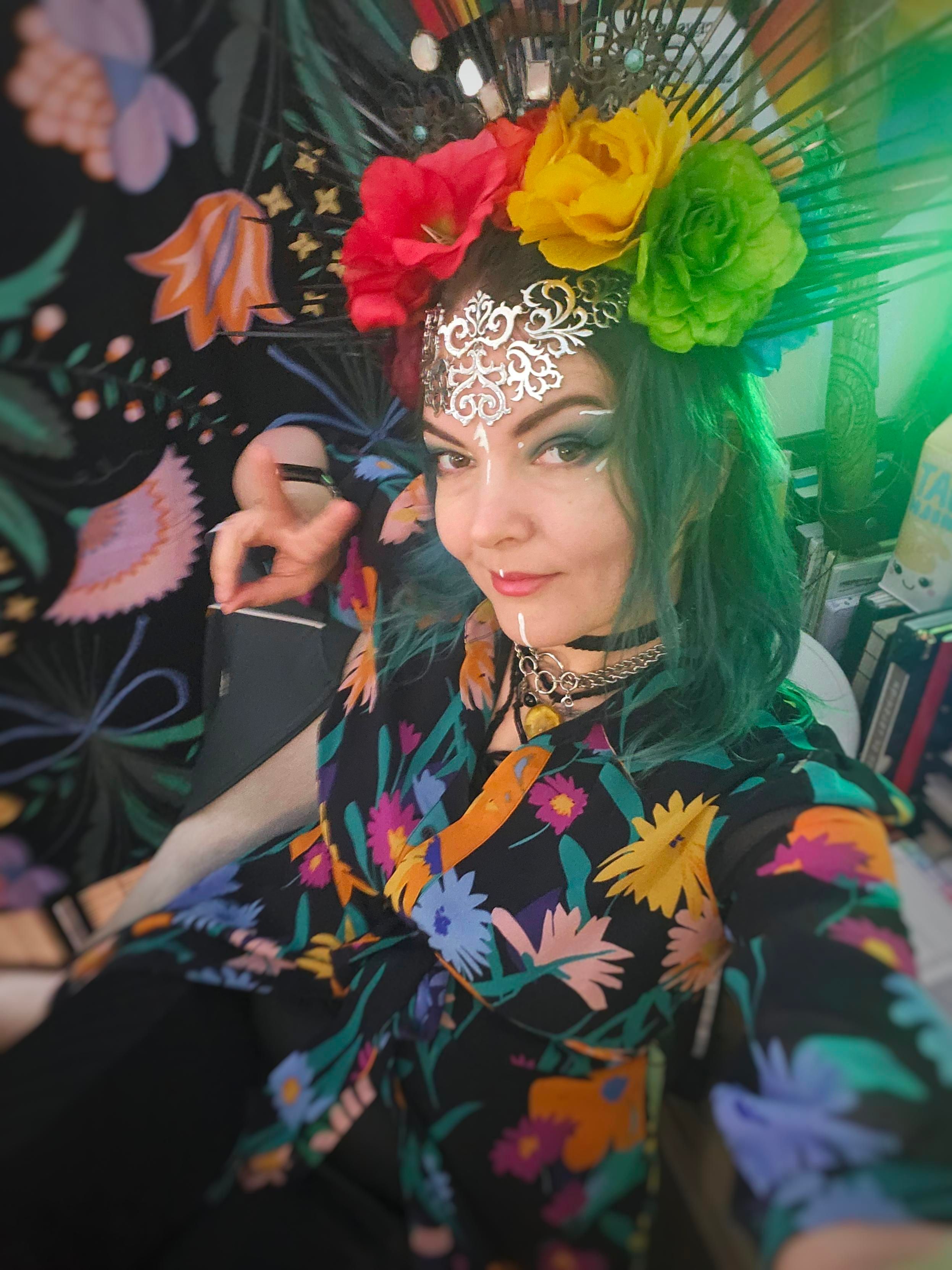 A dressed up and colourful Jen in rainbow flowers and silver jewellery on her forehead. She looks very queer on the internet, which is still legal for now