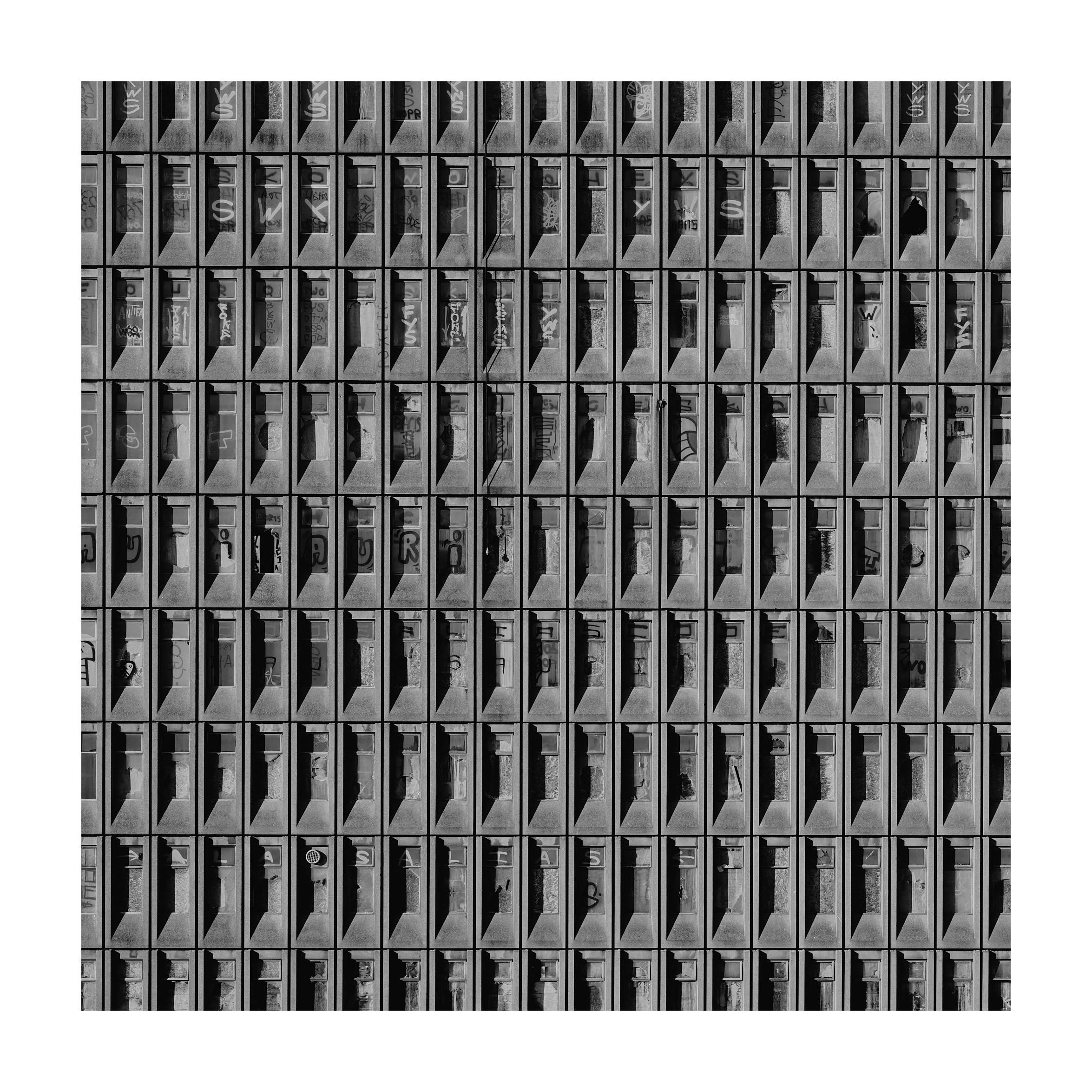 A black and white photo of an old abandoned building with many windows and graffiti.