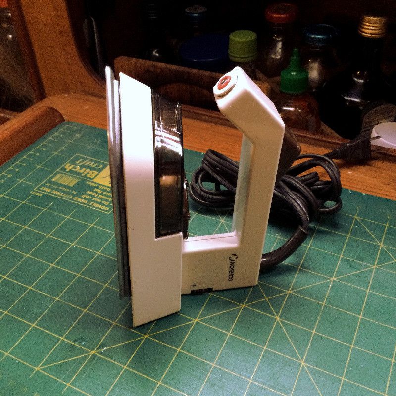 a model TI-70 Philips steam iron laying over a cutting board. The cord is bound by an elastic band. The steam iron handle is in its upright position.