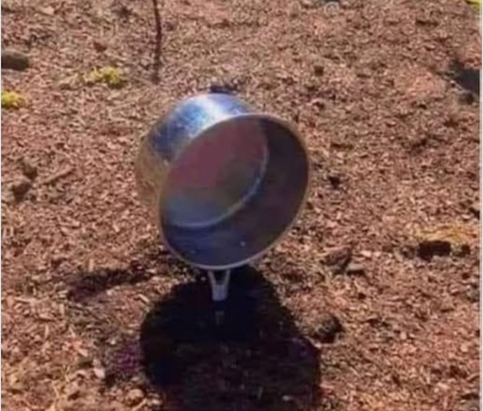 A pot has the handle stuck into freshly tilled earth. 