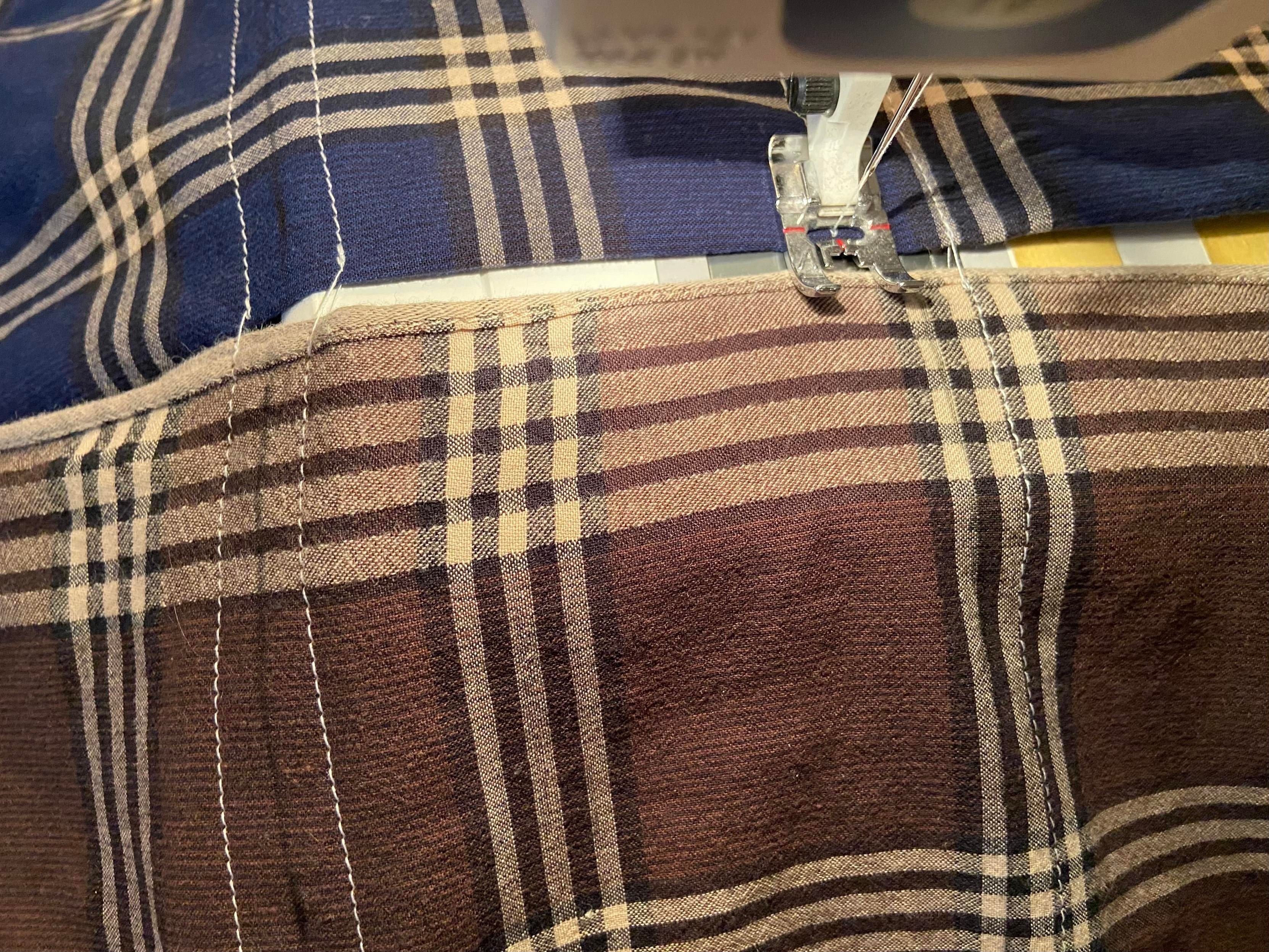 Two handkerchiefs, folded in half, being run through a sewing machine. The sewing machine foot is at the edge of the blue handkerchief and about to move to the brown handkerchief. 