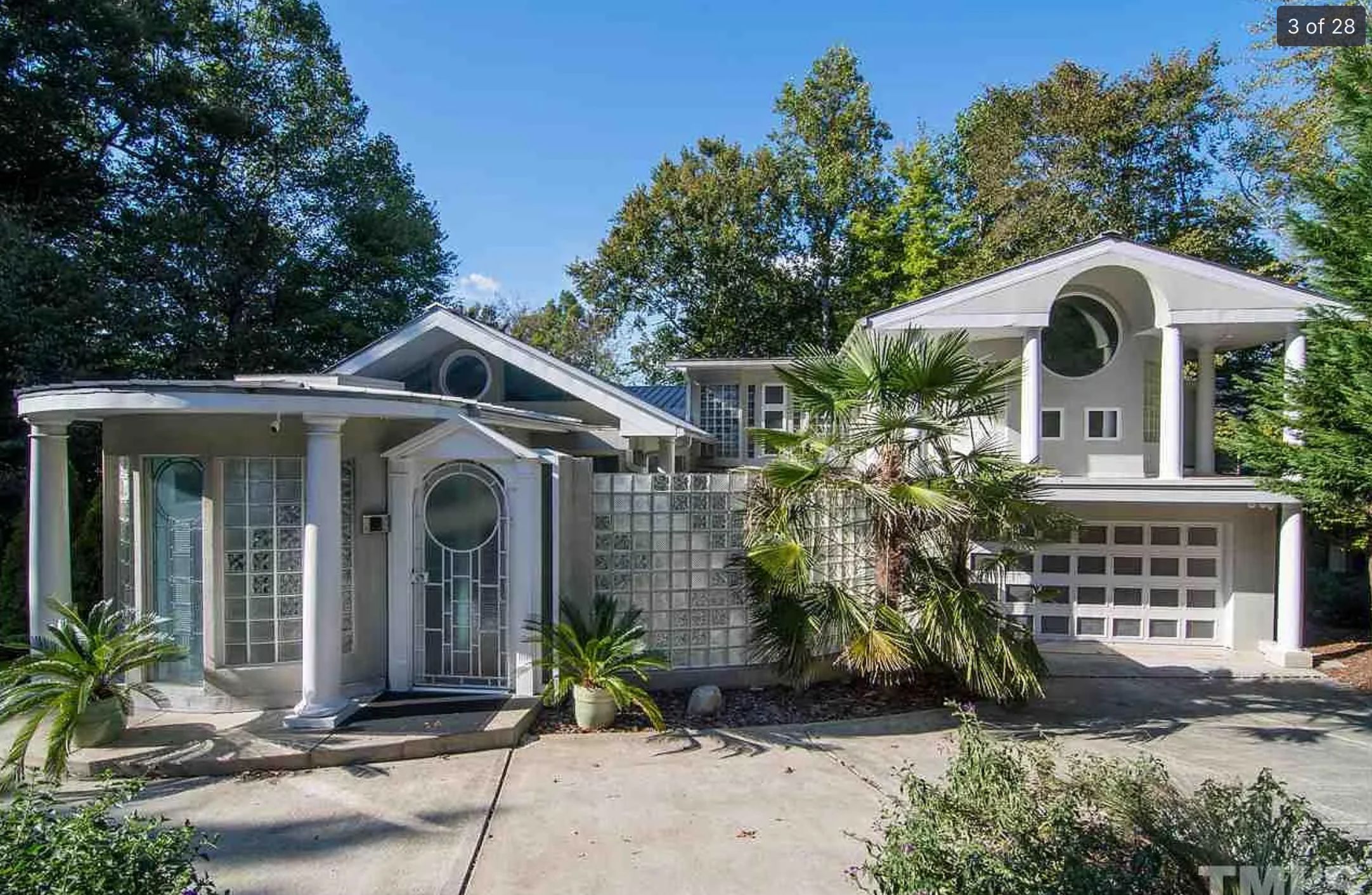 The outside of a very disjointed house with a lot of glass blocks. There are parts that are curved and stick out, other parts with pointed roofs, and a porthole in the 2nd floor. 