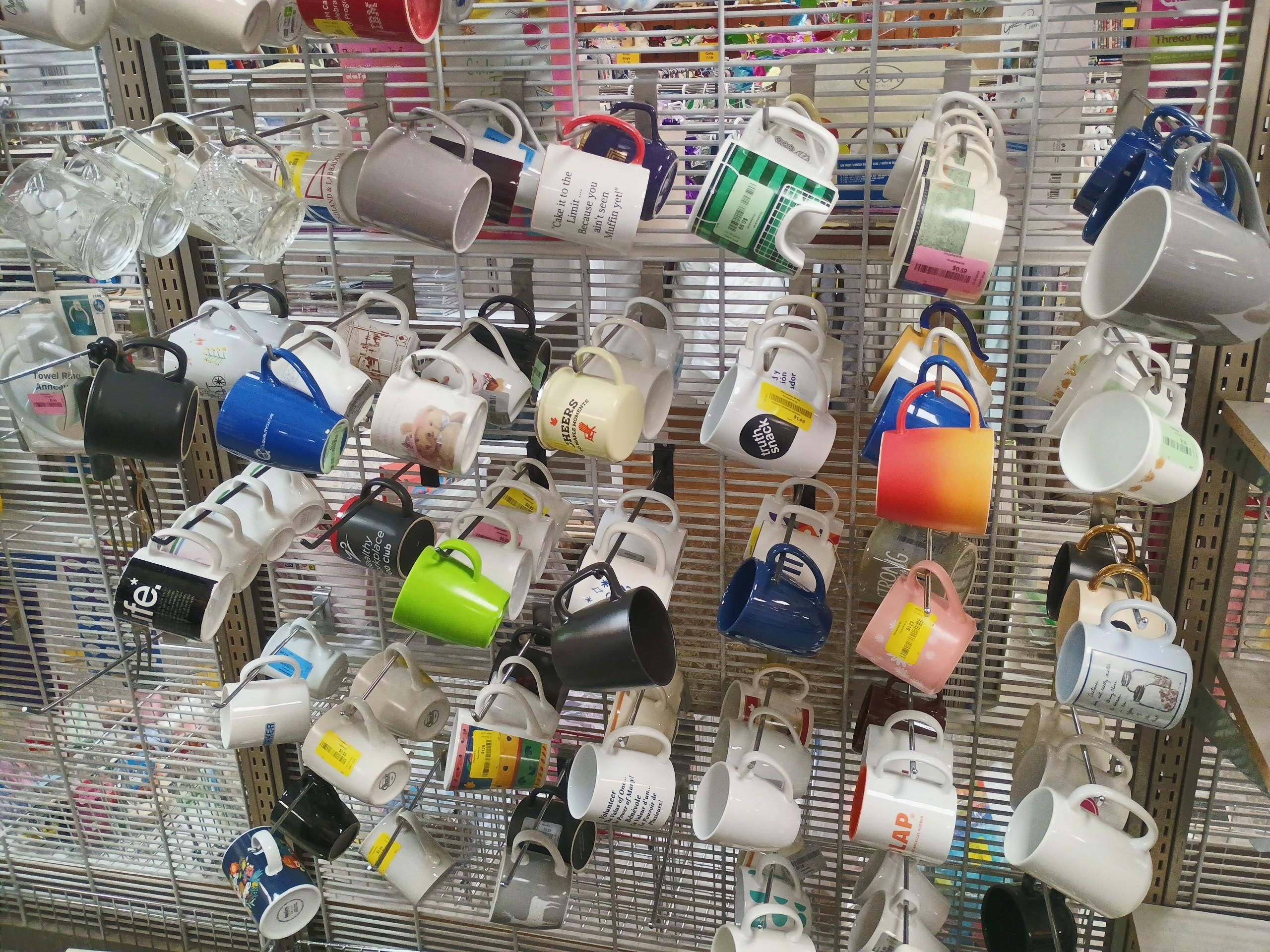 A thrift store display of about fifty or sixty mugs on pegs.
