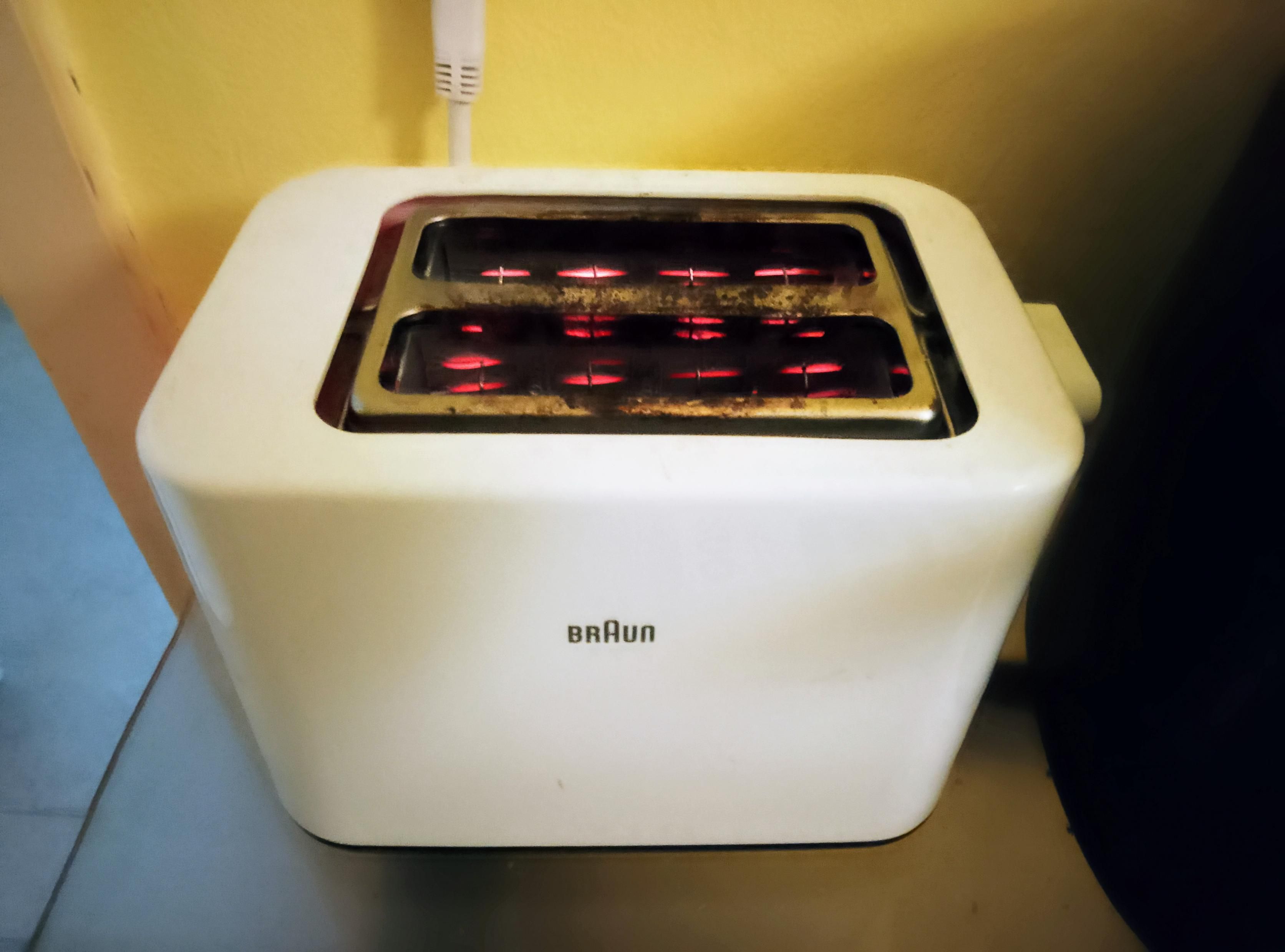 Filaments glow red in a white Braun toaster, as toast toasts inside, round side down. 