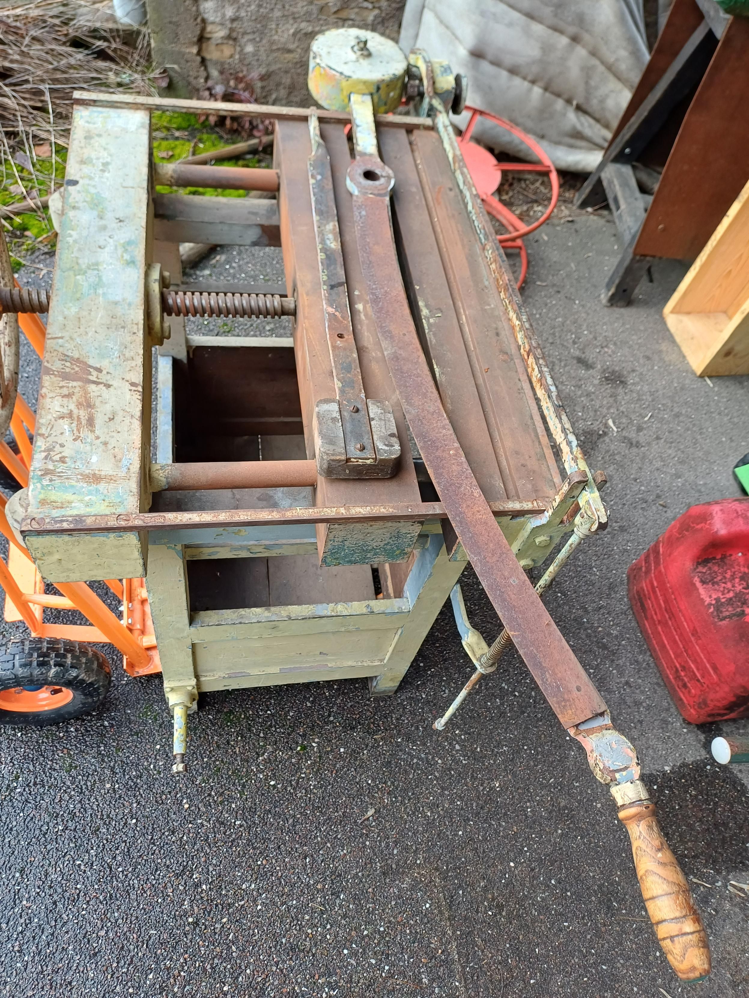 Photo
Combiné à reliure, sur un diable orange.
La partie supérieure est en fonte rouillée avec une manivelle en fonte et une vis pour la partie mobile. Le piètement est en bois peint en gris-vert.
Le massicot, d'environ 1m, est posé sur la table.