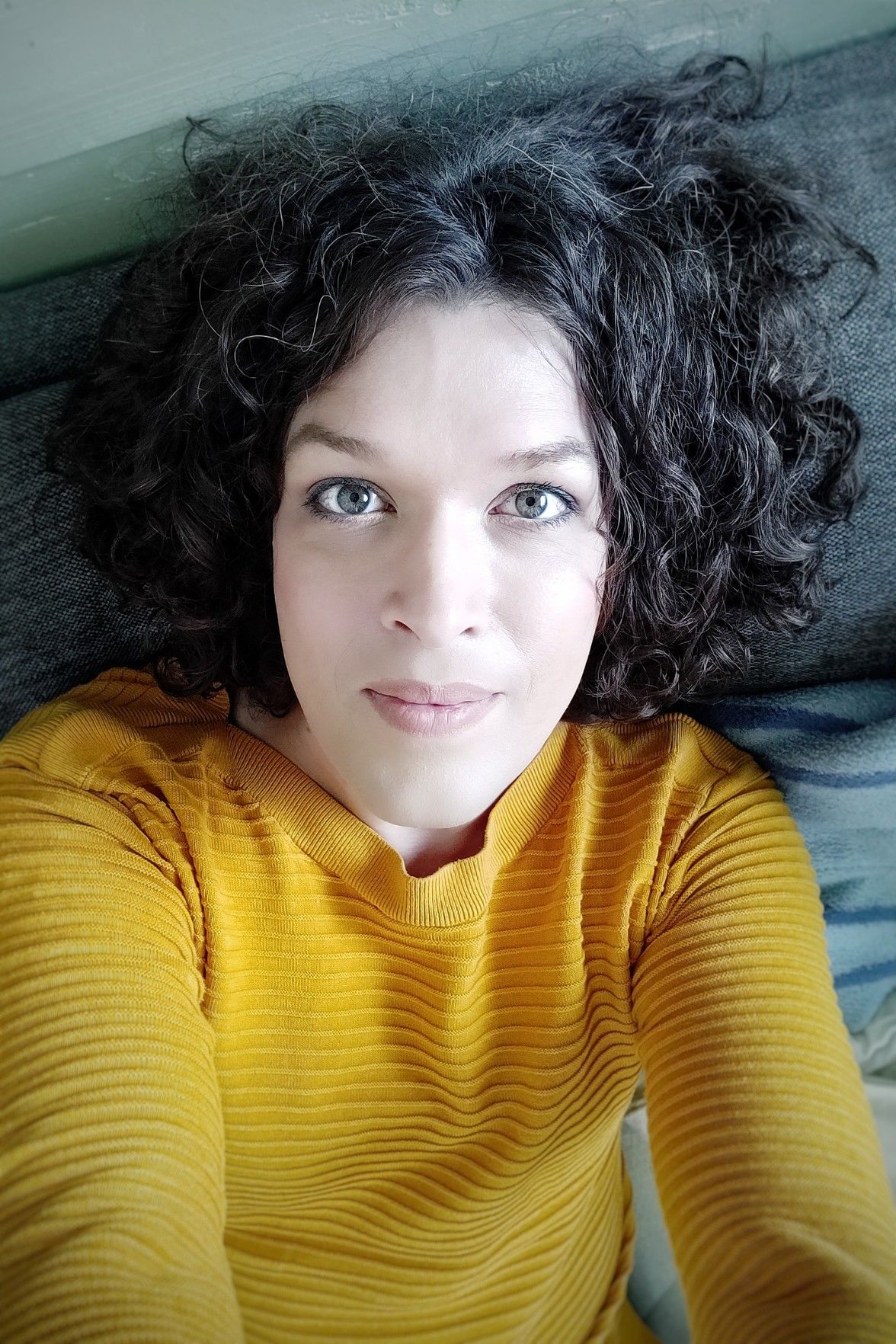 selfie, leaning my head back on the back of the sofa, looking up into the camera smiling, in a yellow shirt.