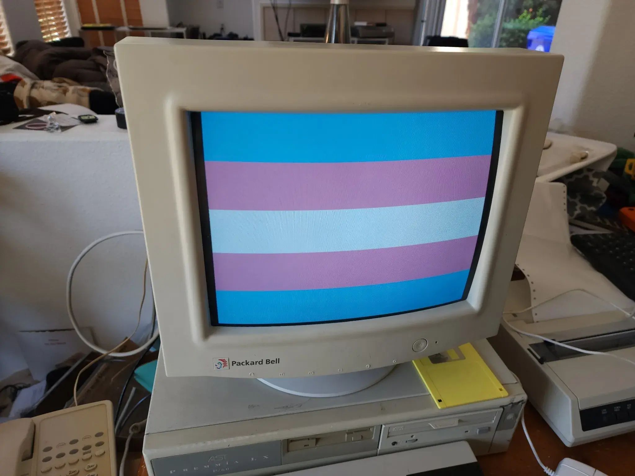 A beige computer from the 90s with a CRT monitor, displaying the trans pride flag